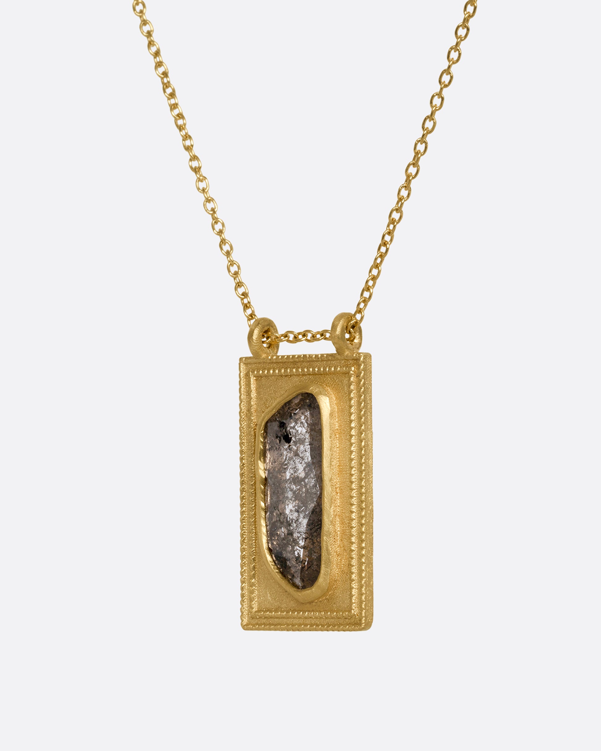 A yellow gold necklace with a rectangular pendant holding a salt and pepper diamond. Shown close up from the side.