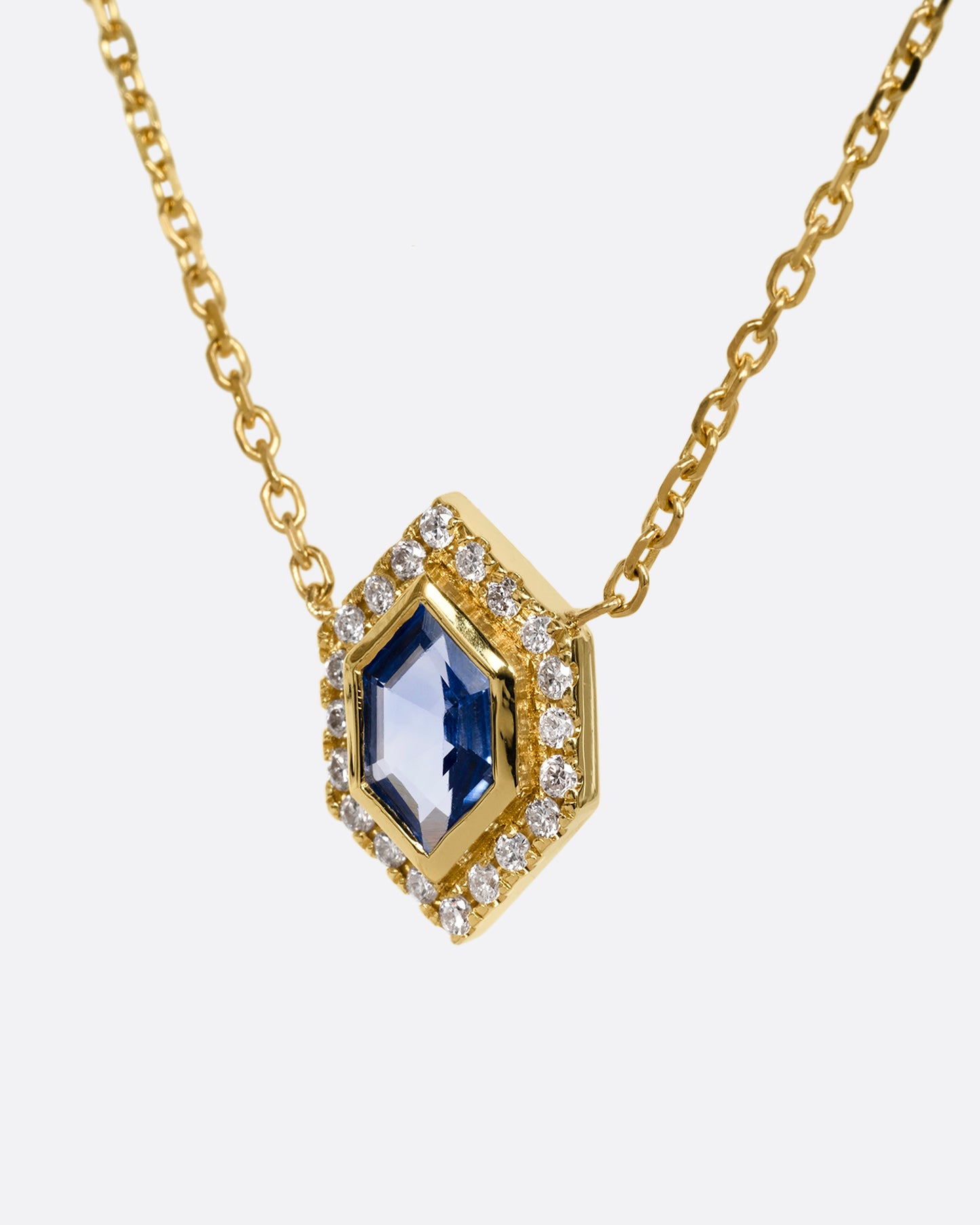 A yellow gold necklace with a hexagon shaped pendant containing a  blue sapphire and diamonds. Shown from the side.