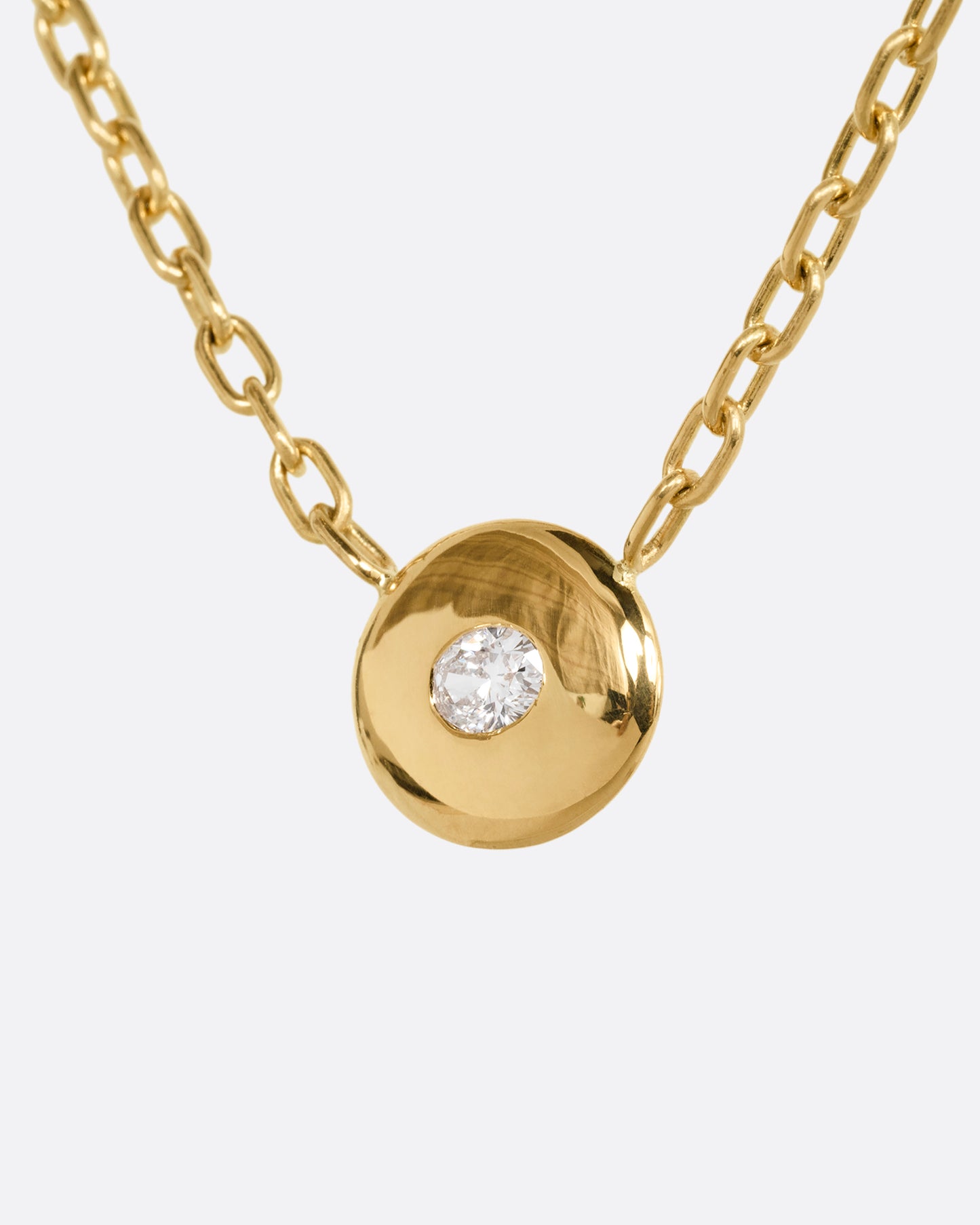 A yellow gold oval pendant necklace with an oval diamond and cable chain. Shown from the side.