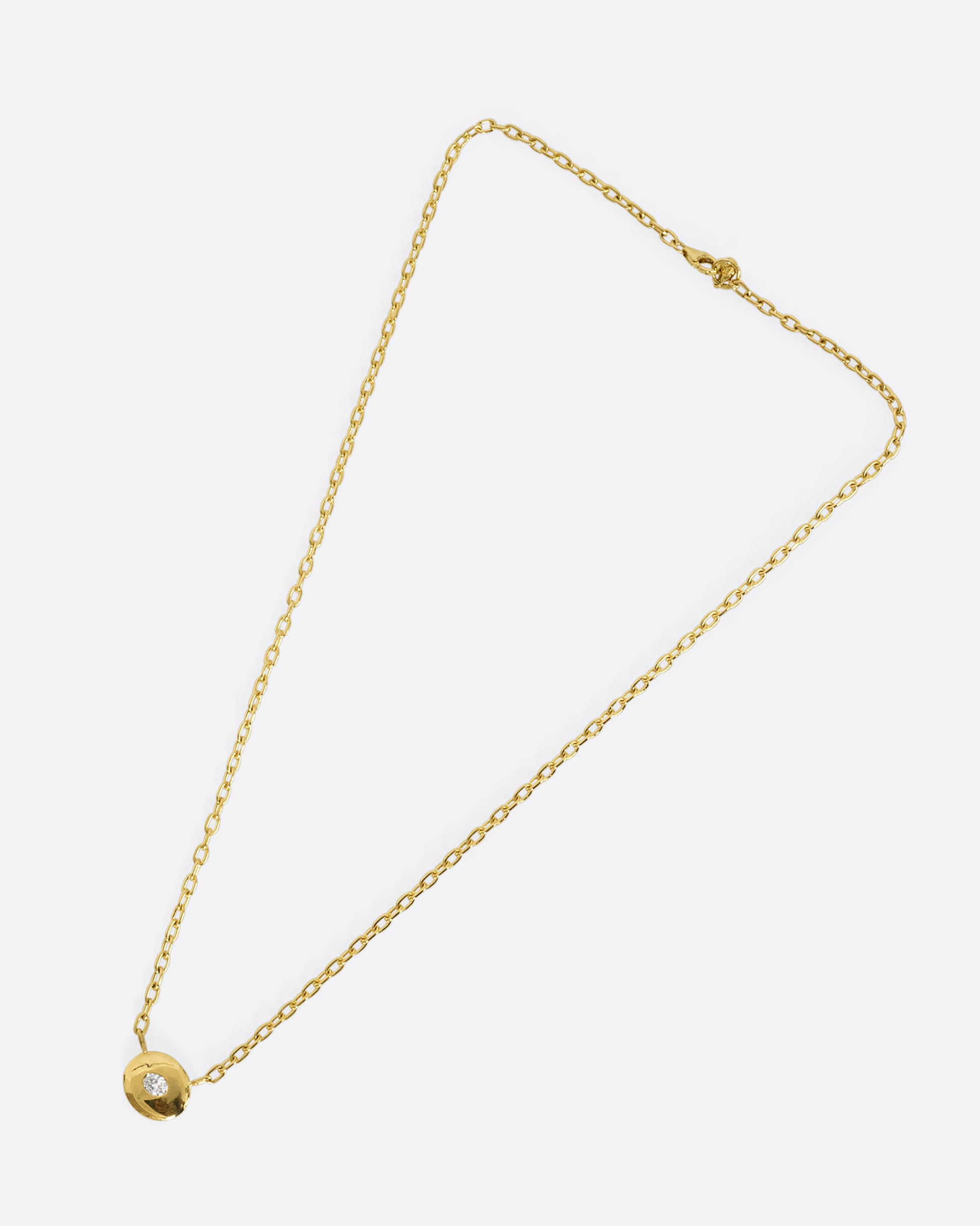 A yellow gold oval pendant necklace with an oval diamond and cable chain. Shown from the front laying flat.