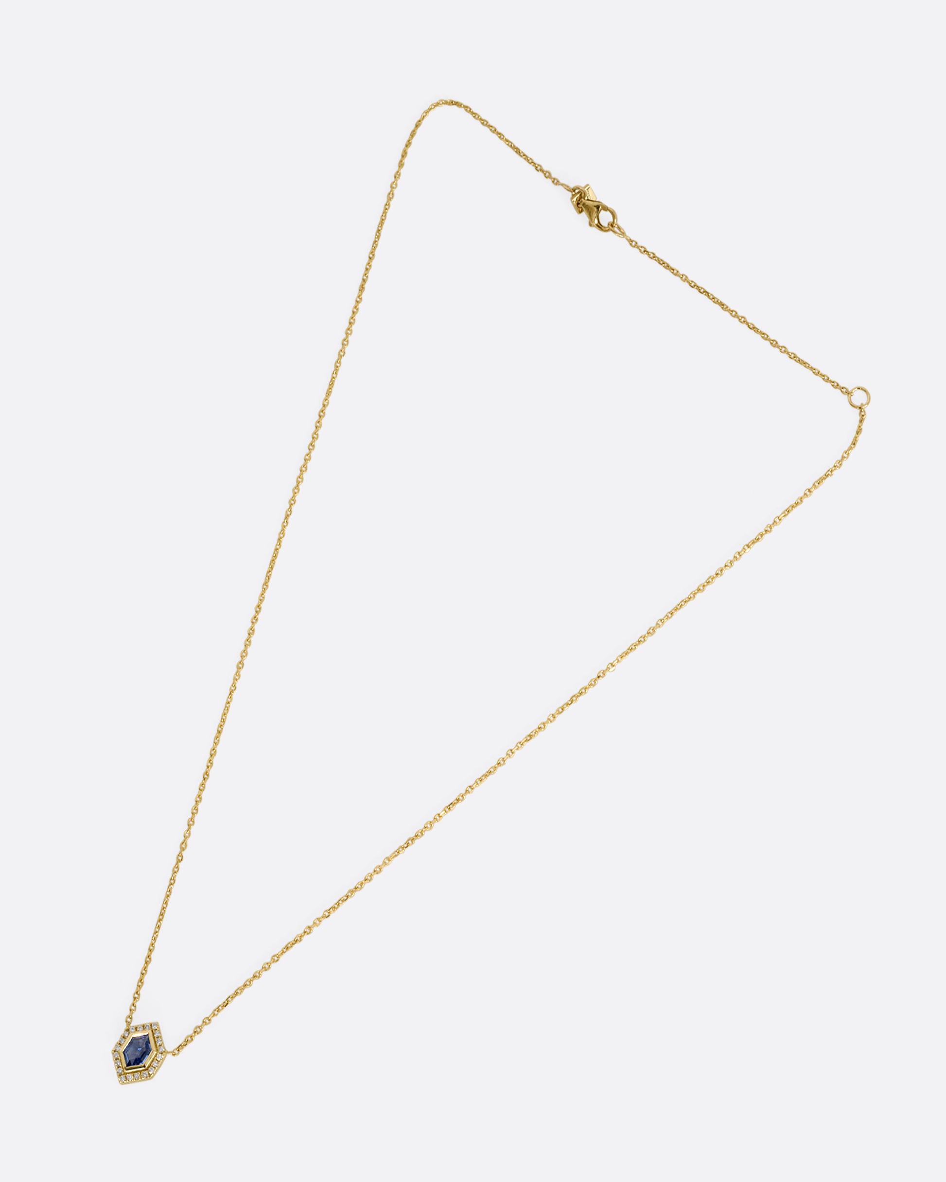 A yellow gold necklace with a hexagon shaped pendant containing a  blue sapphire and diamonds. Shown laying flat.