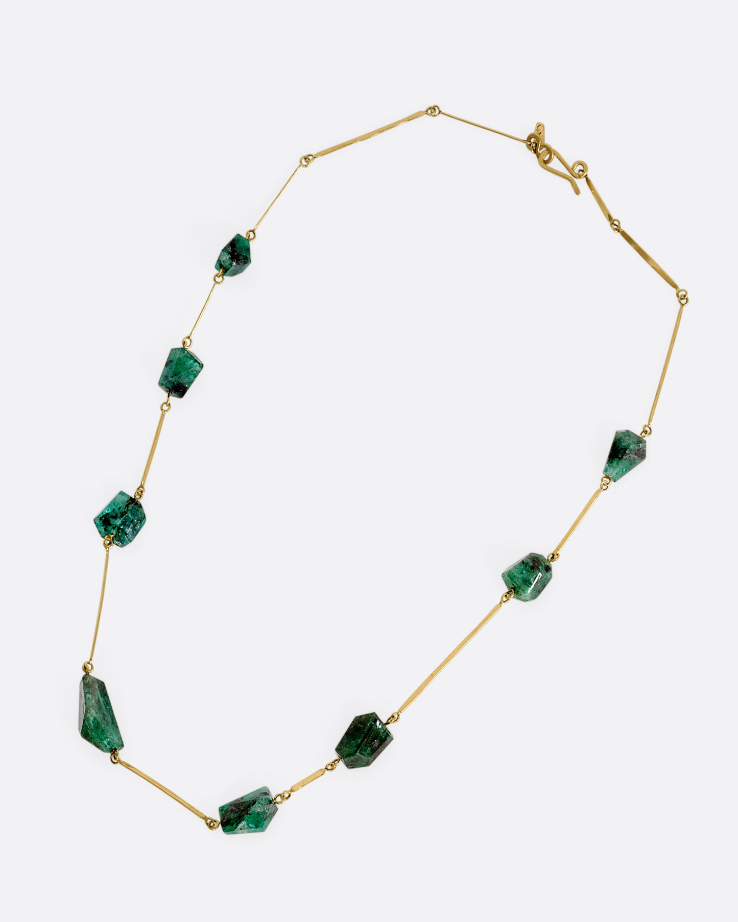 A yellow gold hammered bar link necklace with raw emeralds throughout. Shown laying flat.