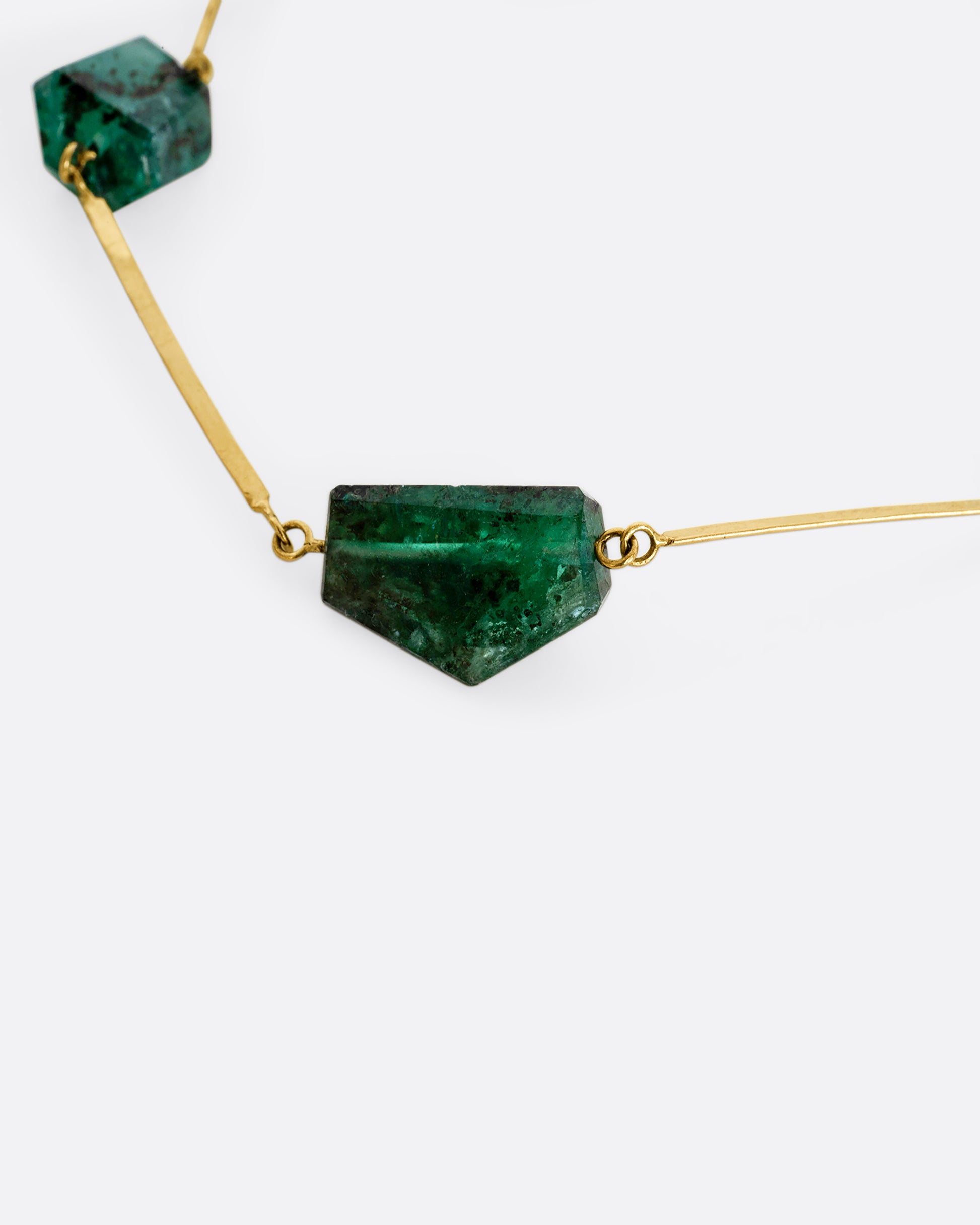 A yellow gold hammered bar link necklace with raw emeralds throughout. Shown close up.