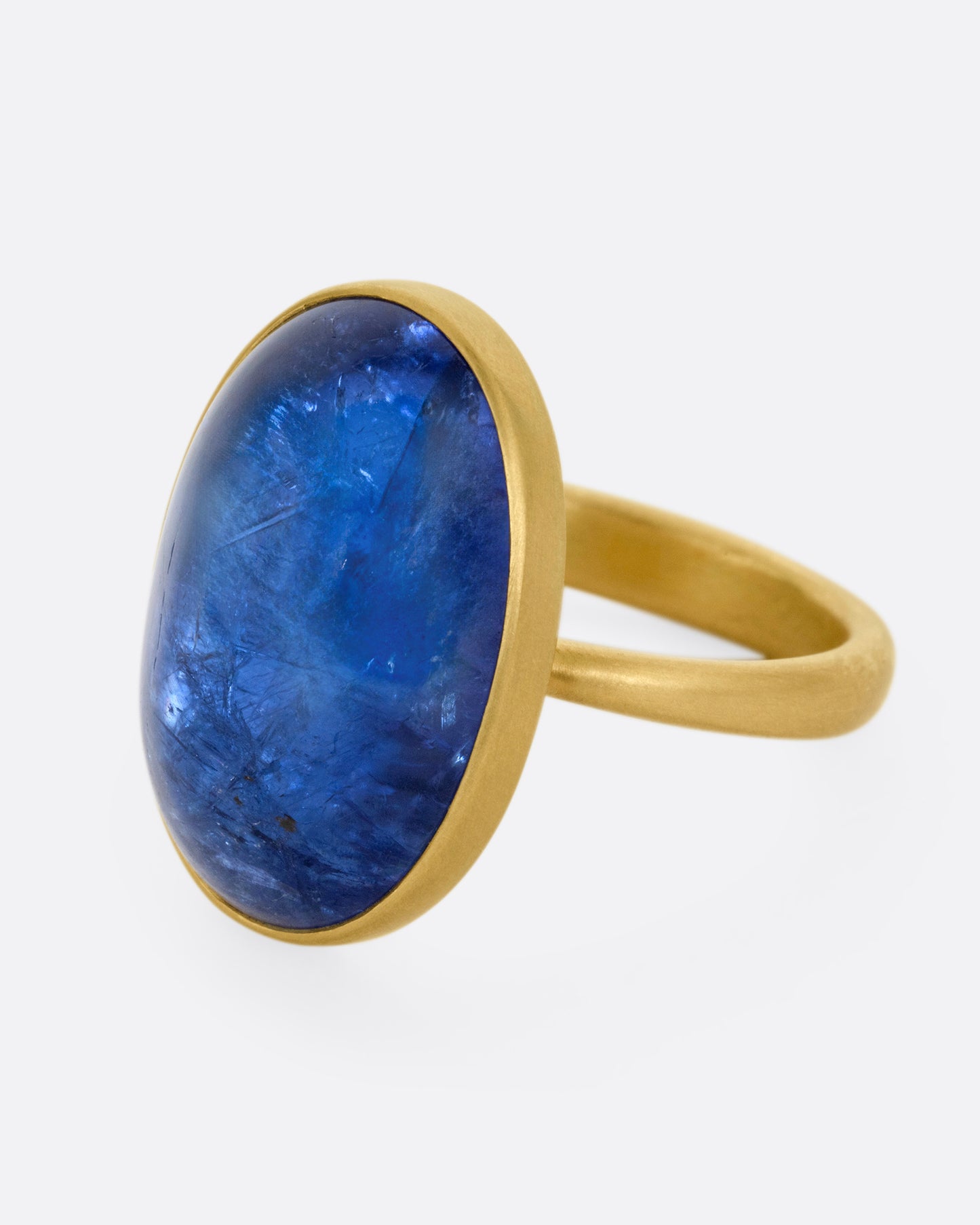 A yellow gold ring with a large blue oval tanzanite, shown from the side.