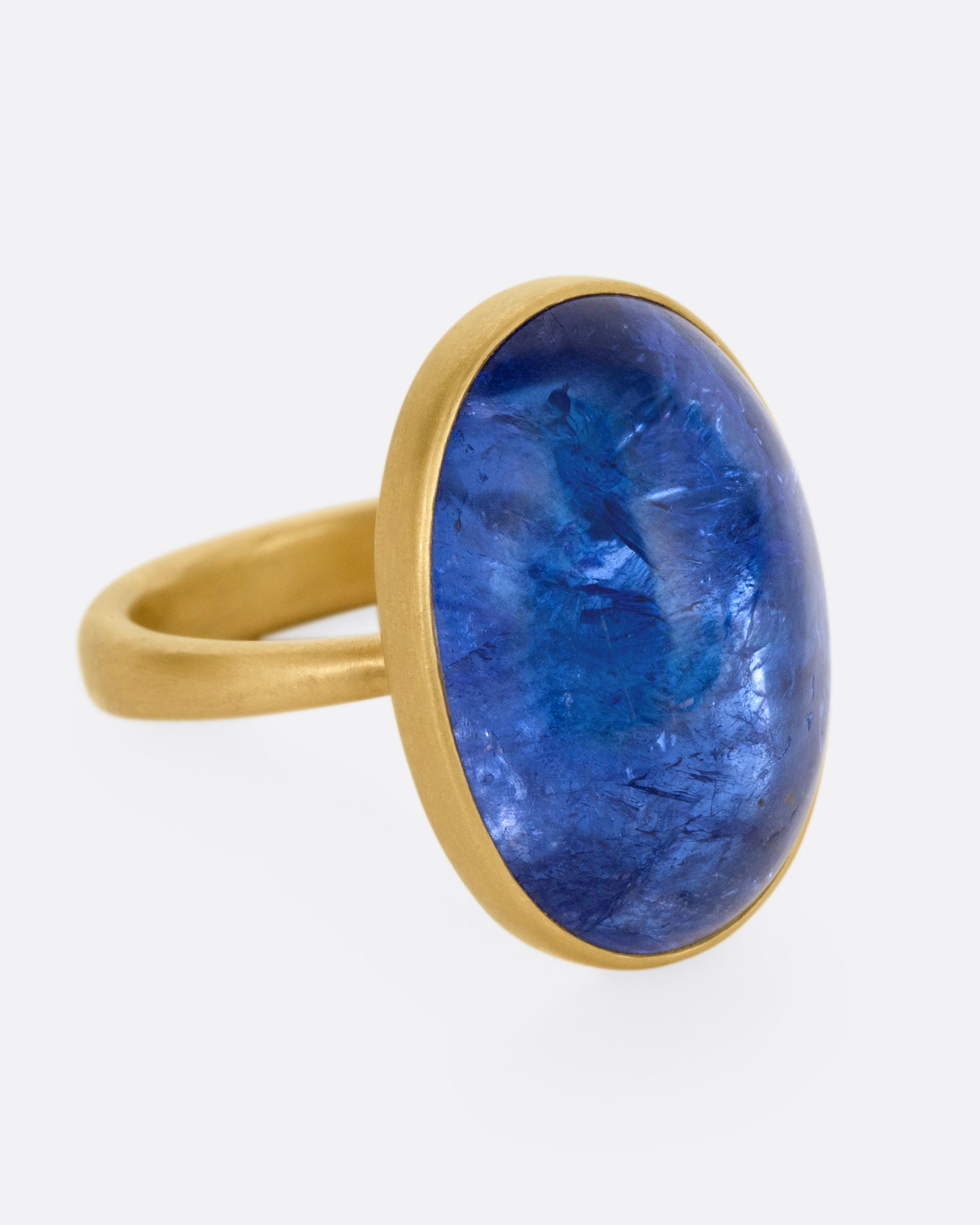 A yellow gold ring with a large blue oval tanzanite, shown from the side.