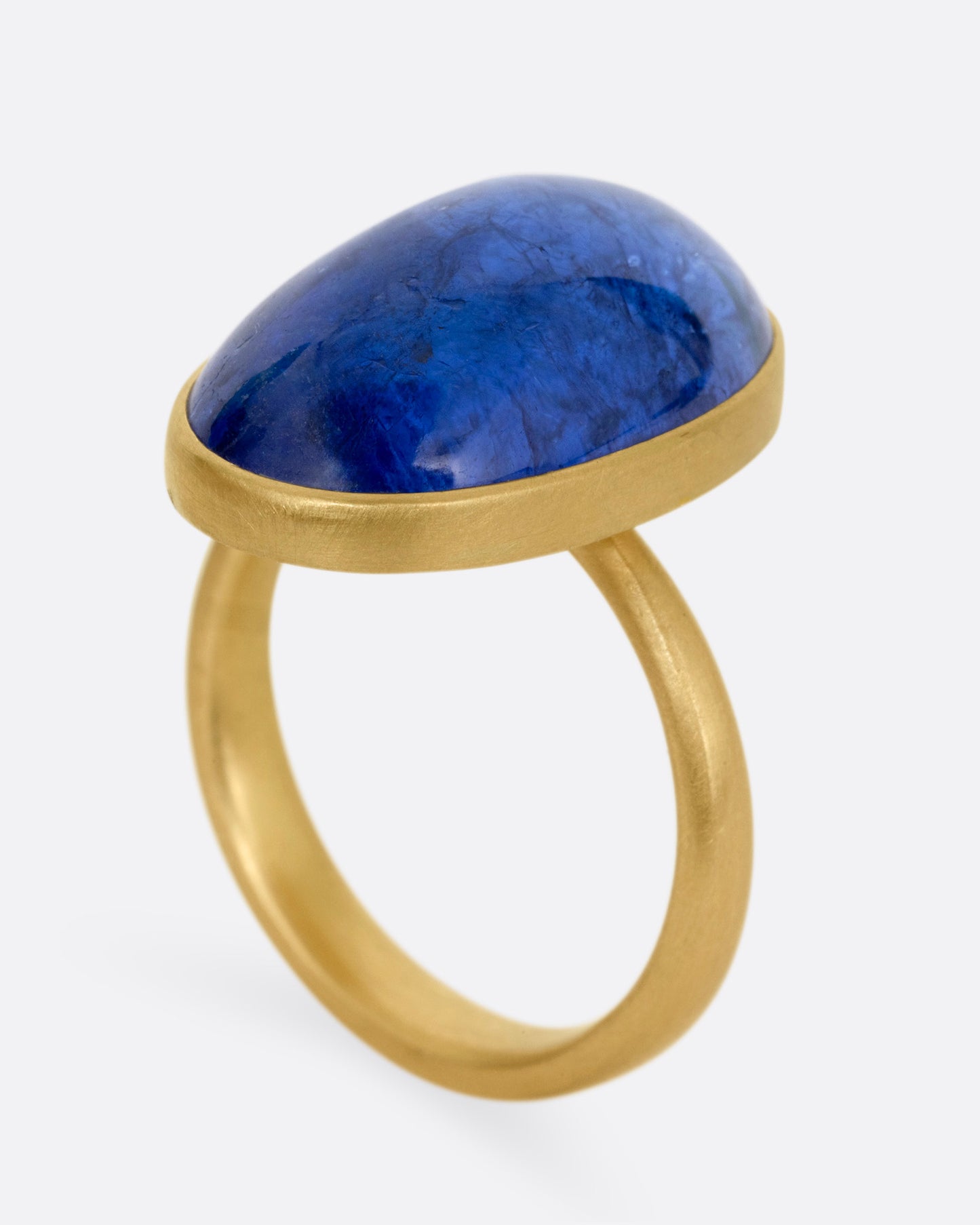 A yellow gold ring with a large blue oval tanzanite, shown from the side standing up.