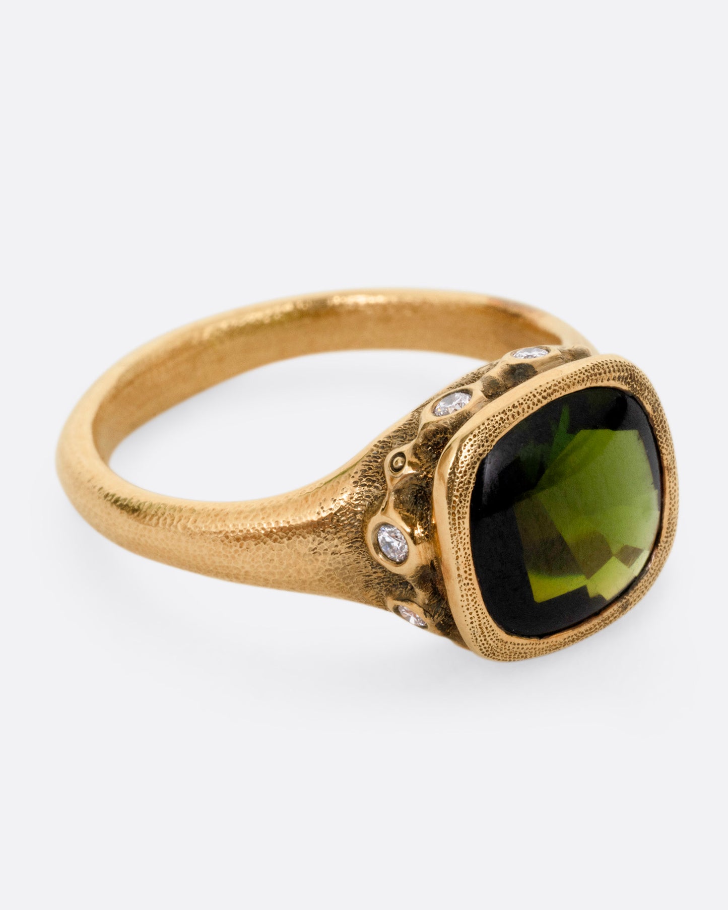 A yellow gold ring with a deep green tourmaline and white diamonds accents around its rounded edges. Shown from the side.