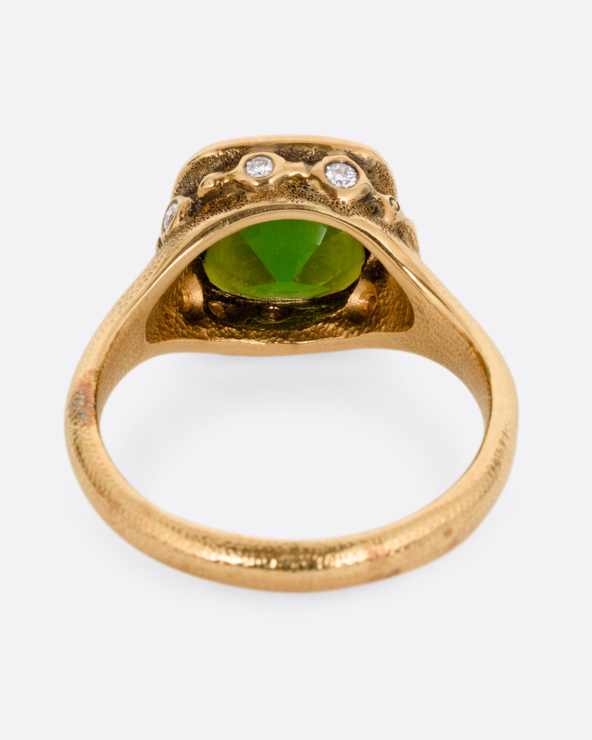 A yellow gold ring with a deep green tourmaline and white diamonds accents around its rounded edges. Shown from the back.