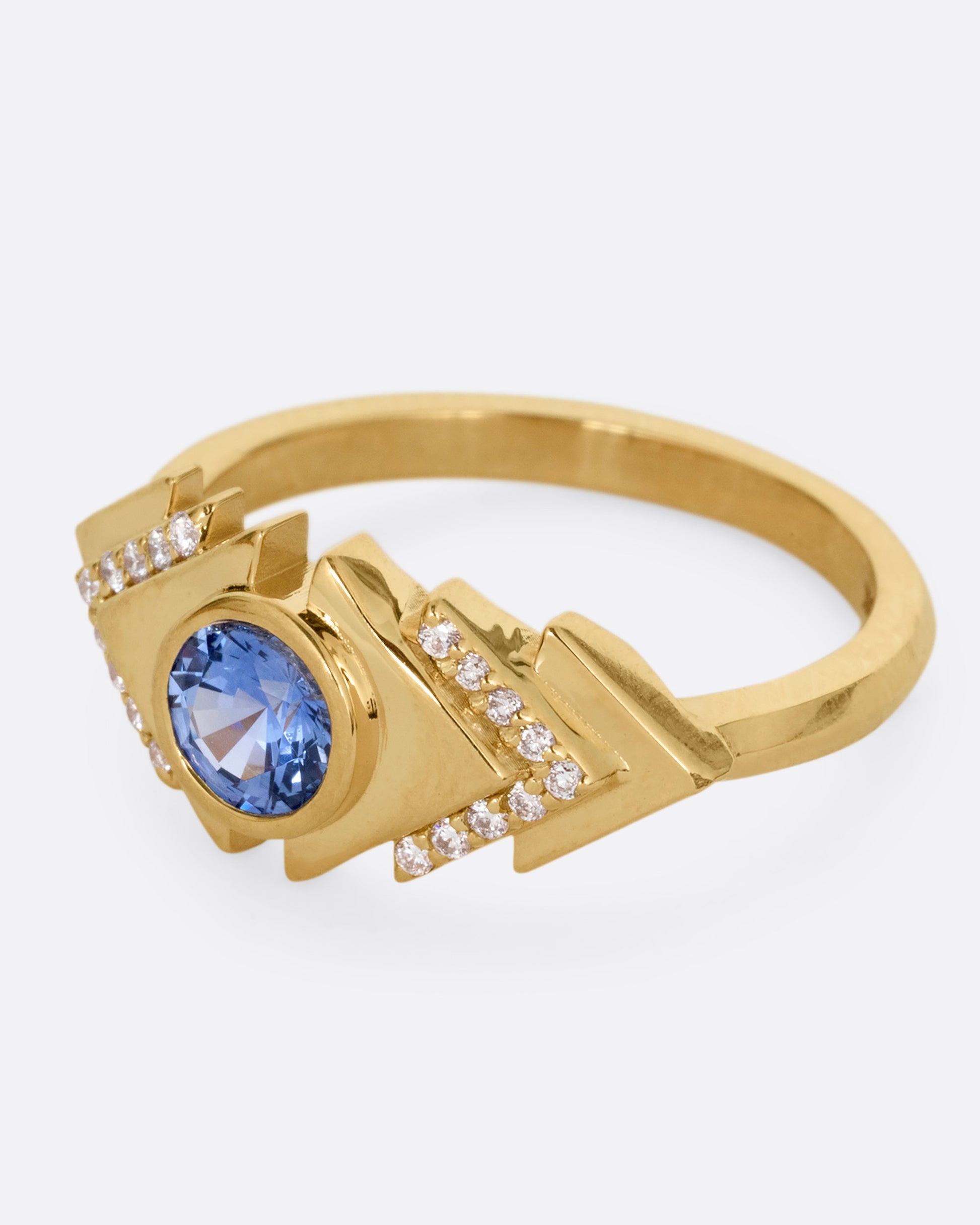 A yellow gold ring with a blue sapphire at the center of angular steps with diamond accents, shown from the side.