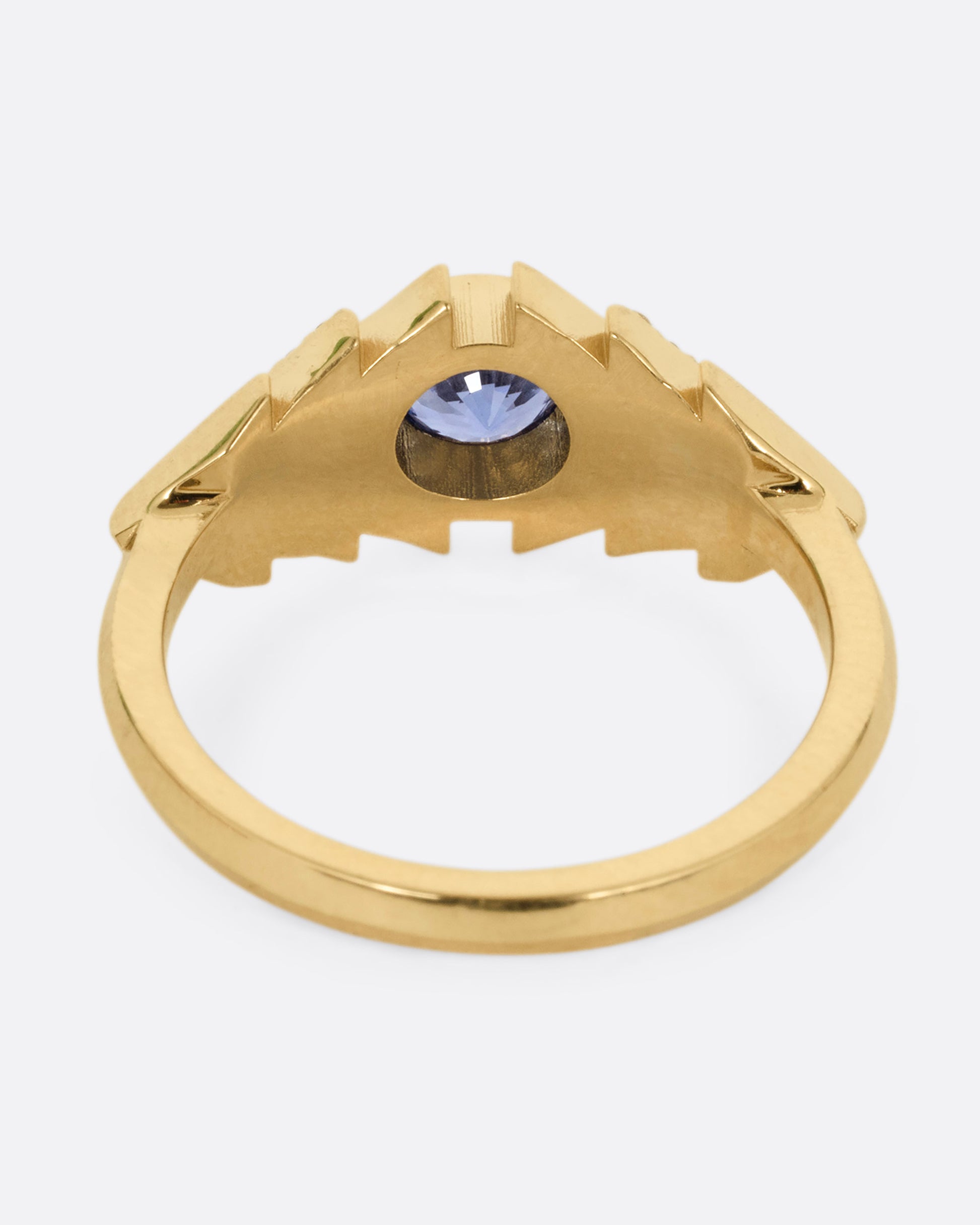 A yellow gold ring with a blue sapphire at the center of angular steps with diamond accents, shown from the back.