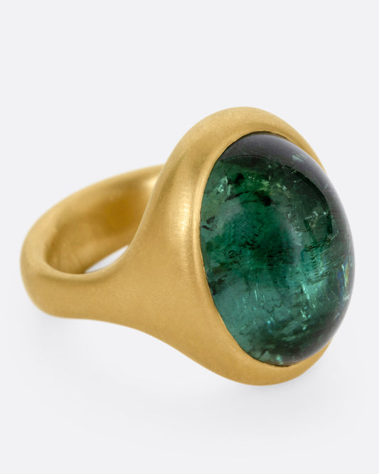 A yellow gold ring with a green tourmaline cabochon, shown from the side.