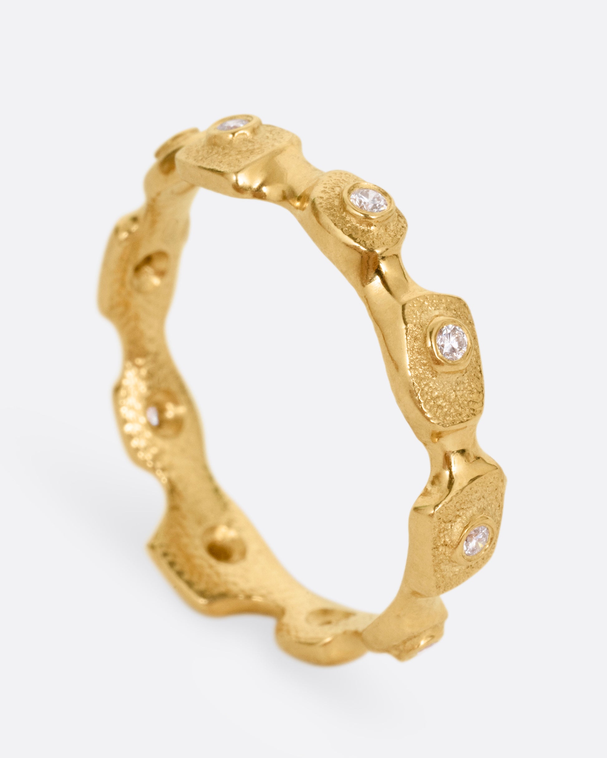 A yellow gold ring with stations of single diamonds, shown from the side standing up.