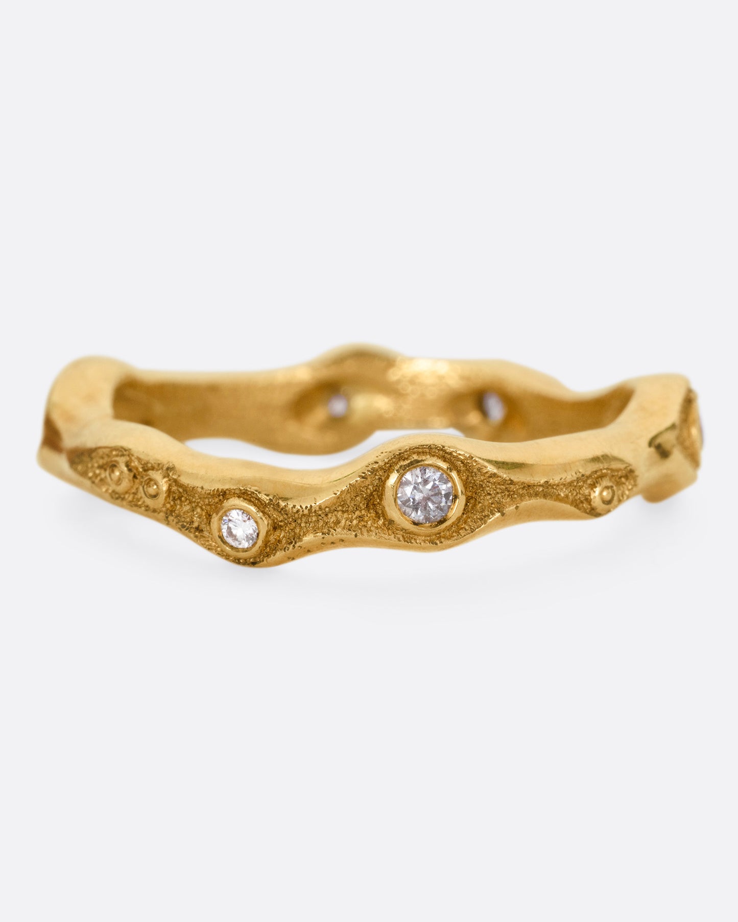 A textured yellow gold band in a fluid shape with white diamonds, shown from the front.