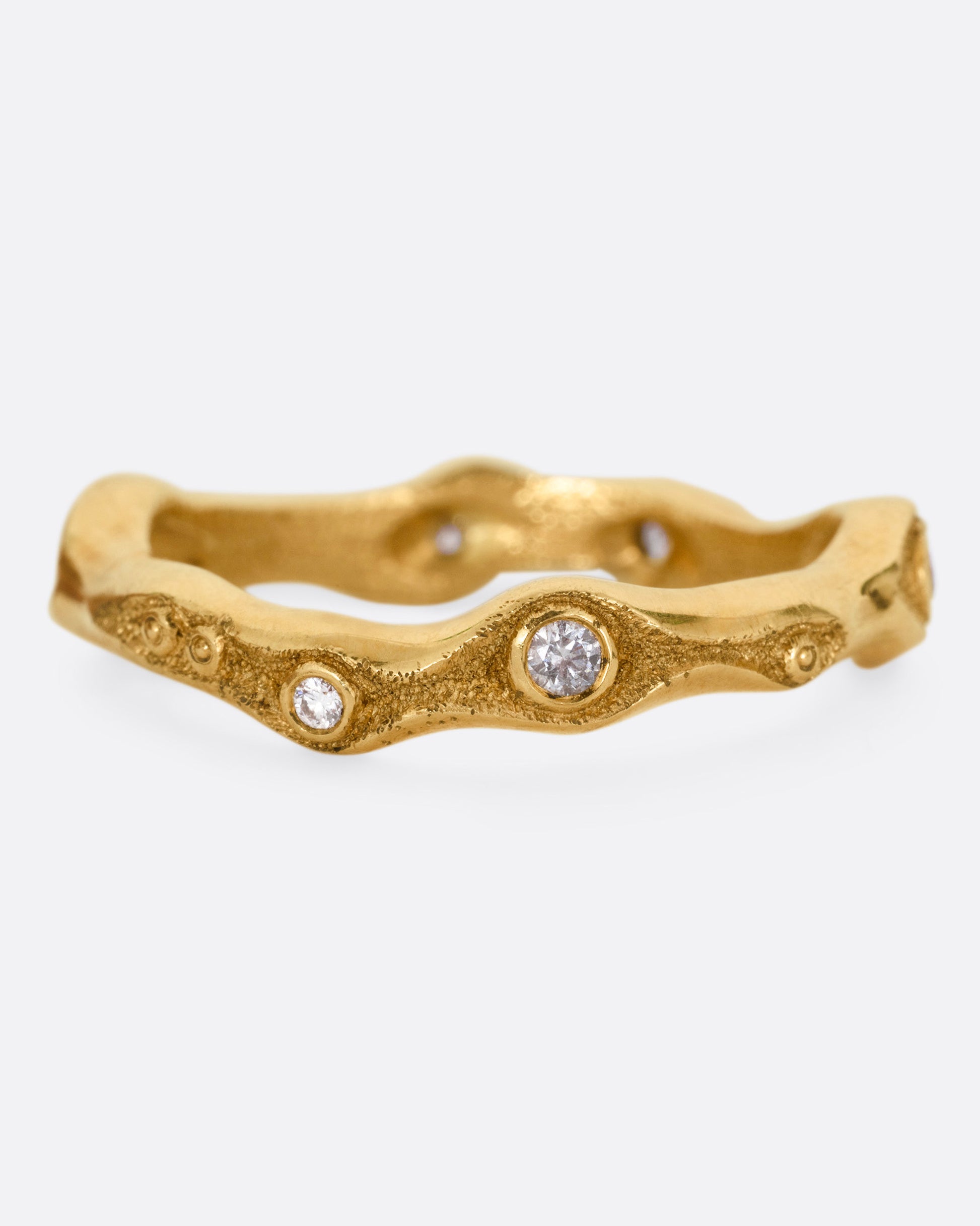 A textured yellow gold band in a fluid shape with white diamonds, shown from the front.