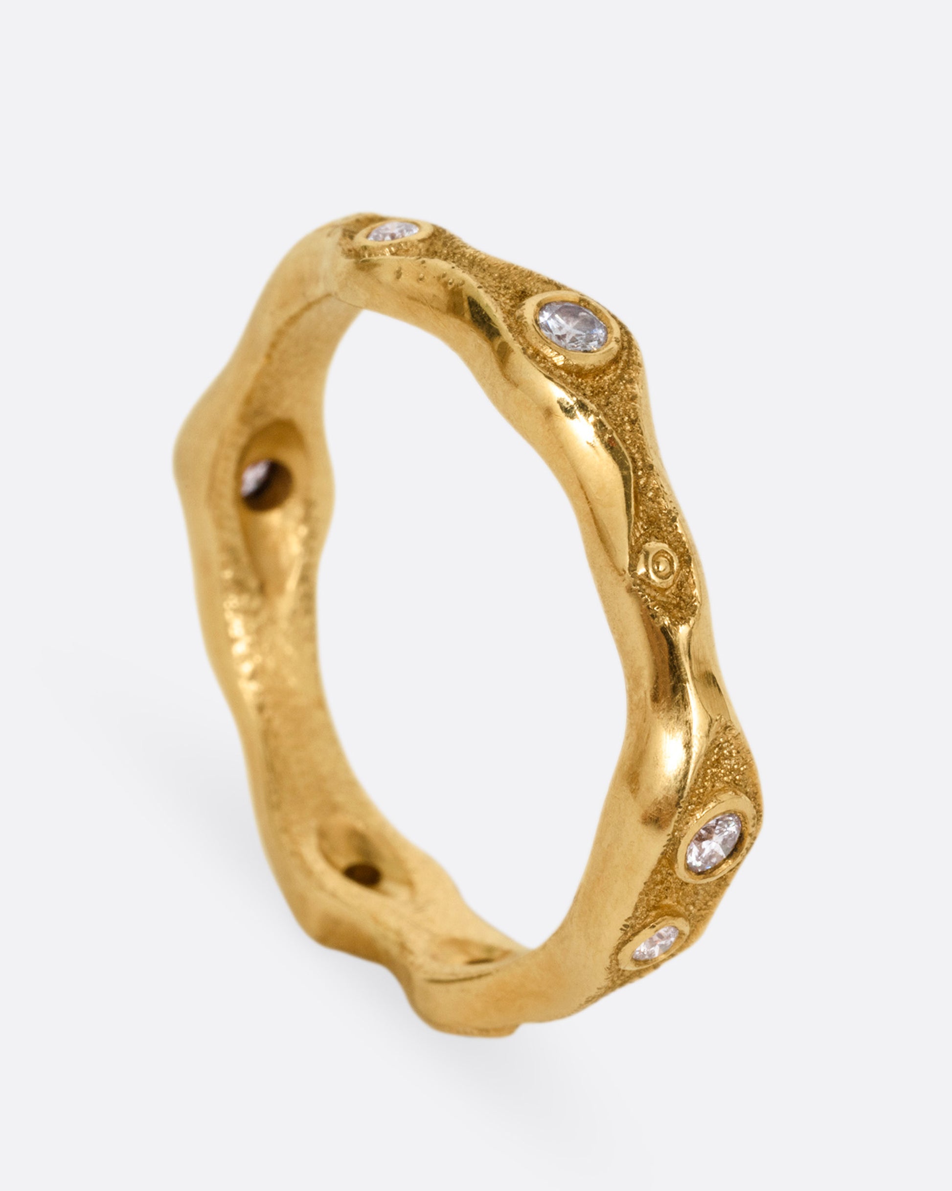 A textured yellow gold ring with white diamonds. Shown from the side standing up.