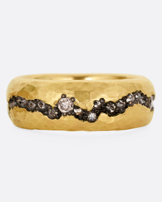 A yellow gold hammered ring with a fissure lined with brown and white diamonds, some reverse set, shown from the front.