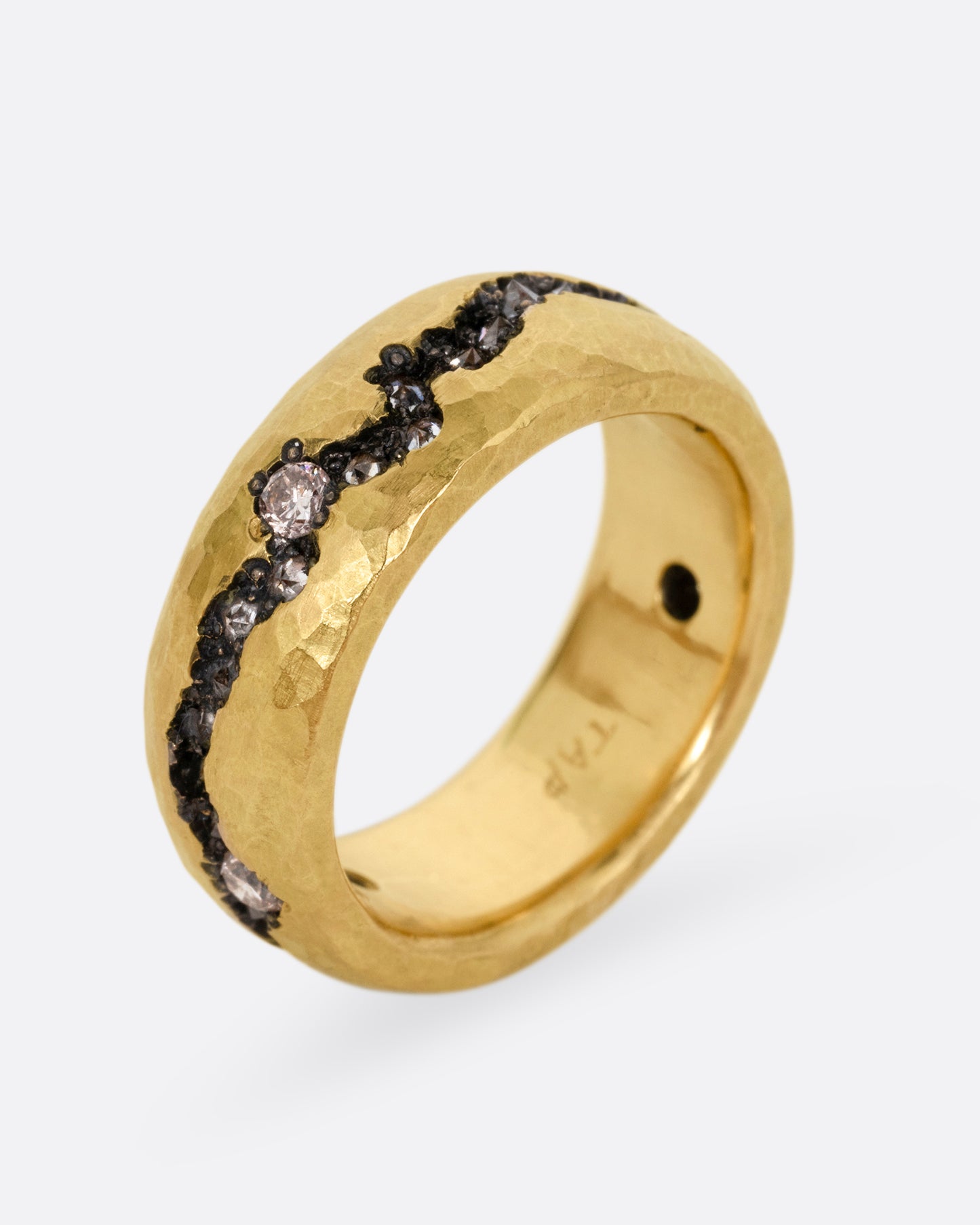 A yellow gold hammered ring with a fissure lined with brown and white diamonds, some reverse set, shown from the side standing up.