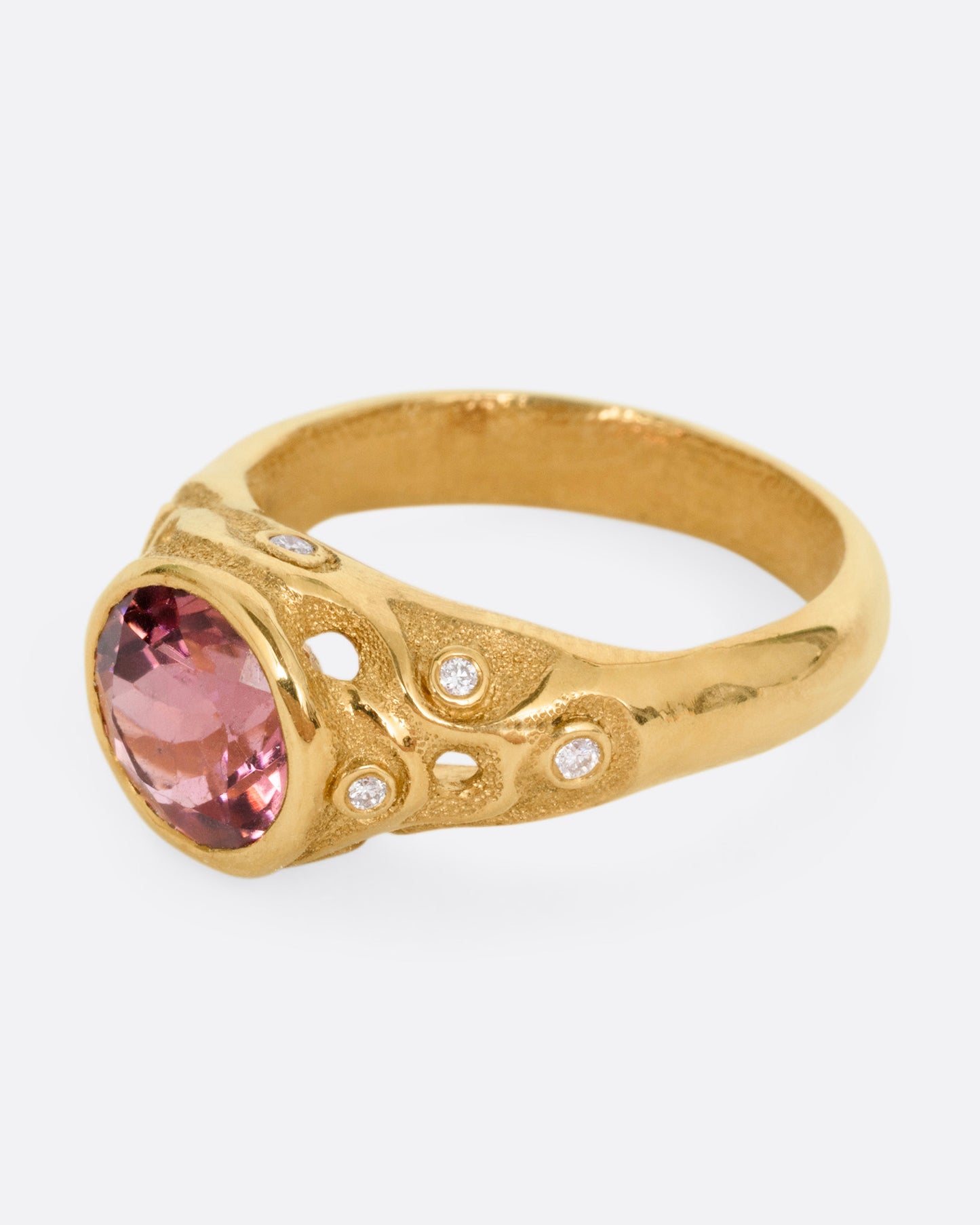 A yellow gold ring with a rose cut pink tourmaline and diamond freckled shoulders, shown from the side.