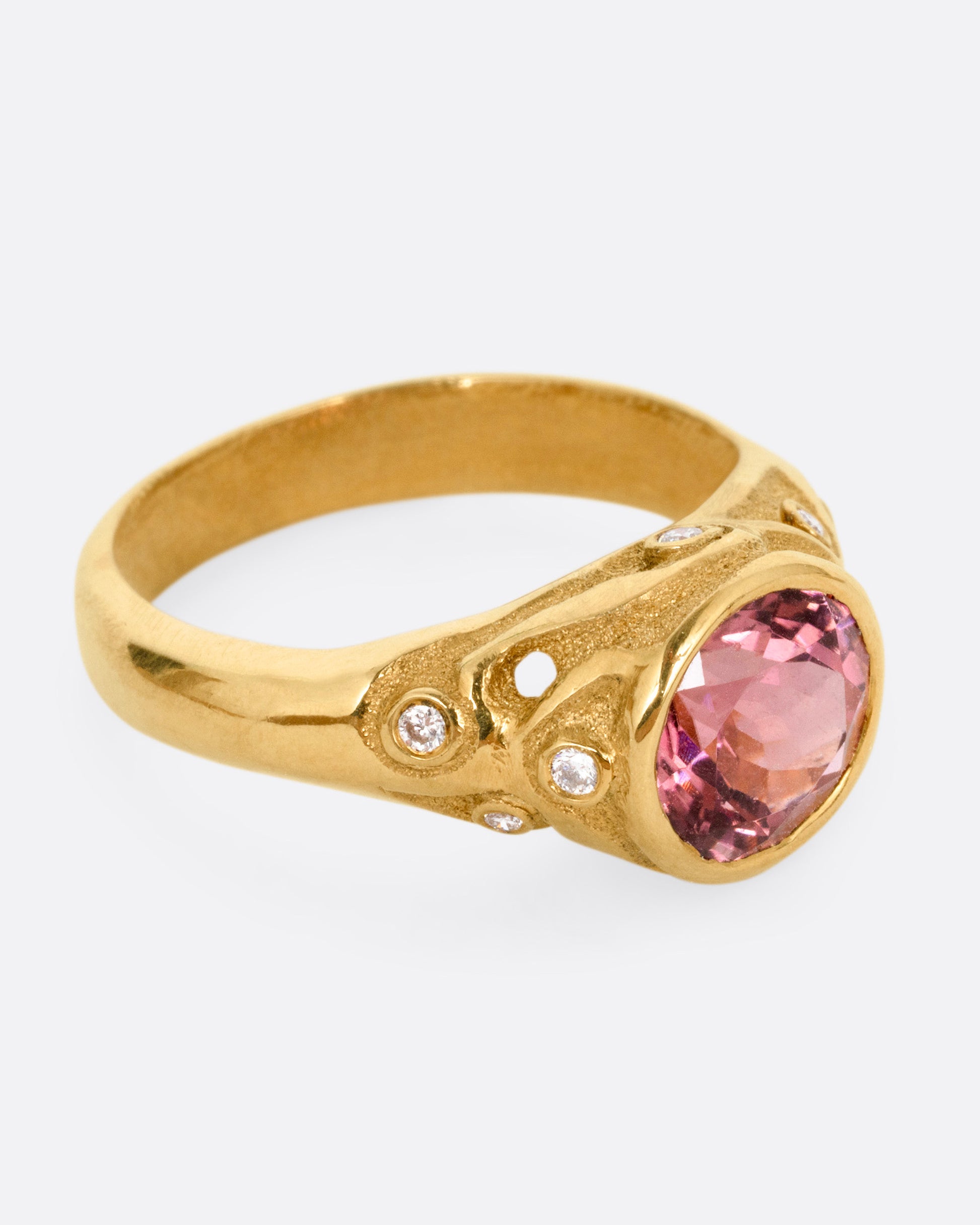 A yellow gold ring with a rose cut pink tourmaline and diamond freckled shoulders, shown from the side.