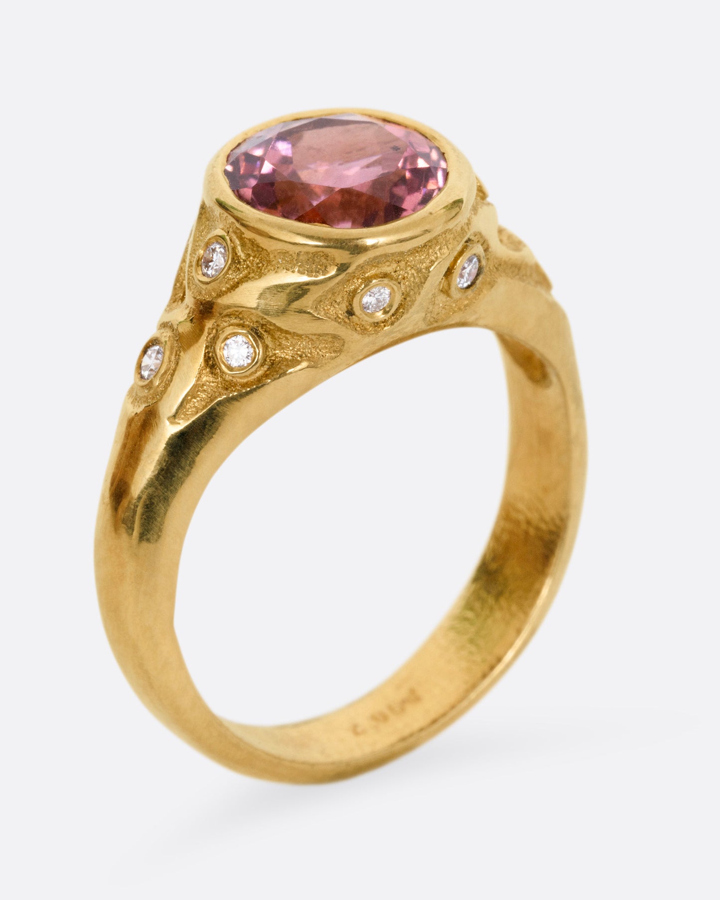 A yellow gold ring with a rose cut pink tourmaline and diamond freckled shoulders, shown from the side standing up.
