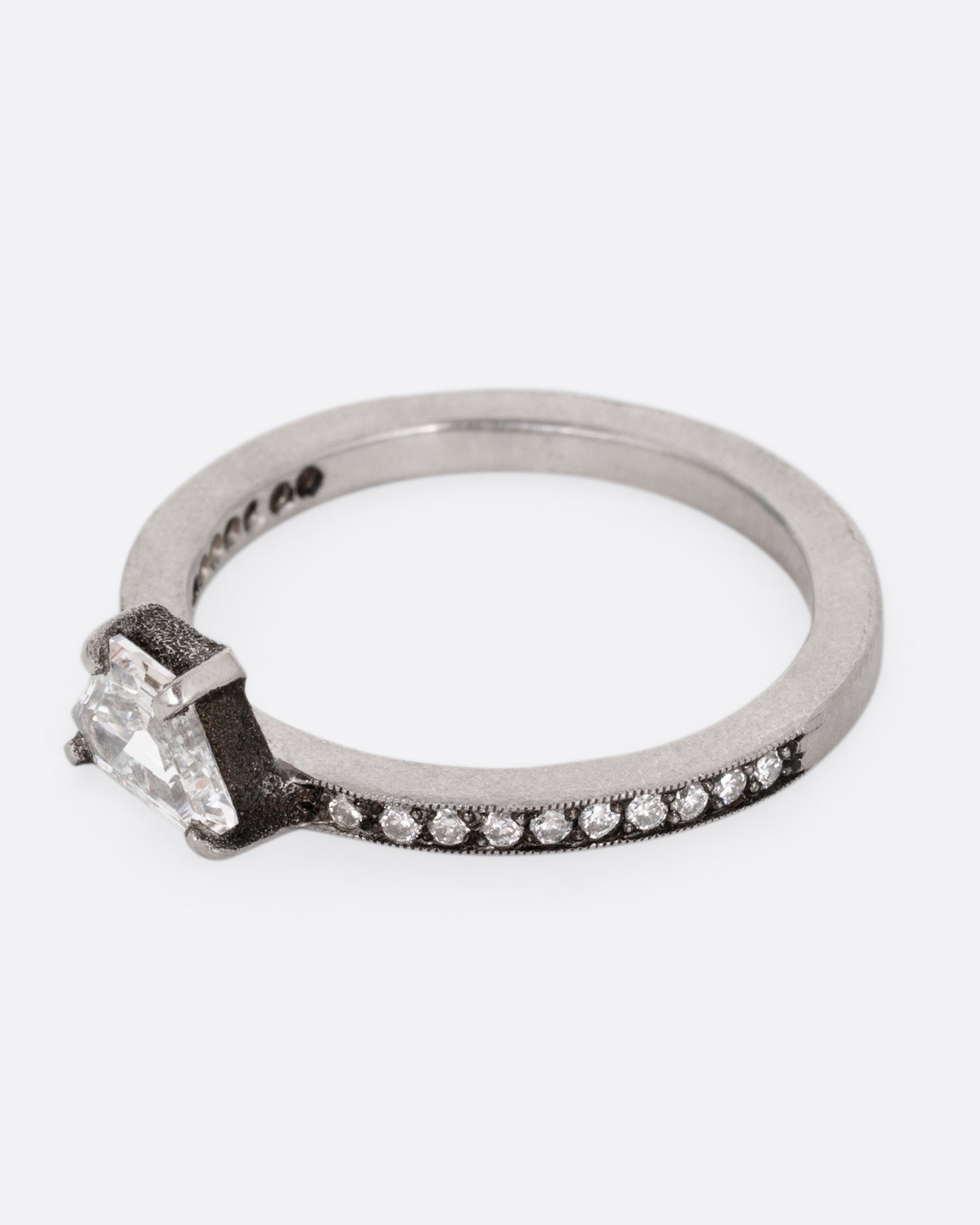 A platinum band with pave diamonds all the way around and a solitaire trapeze diamond. Shown from the side.