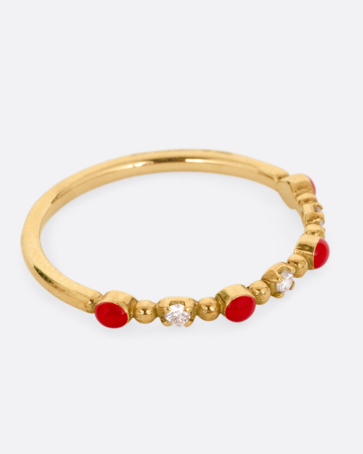 A yellow gold ring with three white diamonds and four red resin droplets, shown from the side.