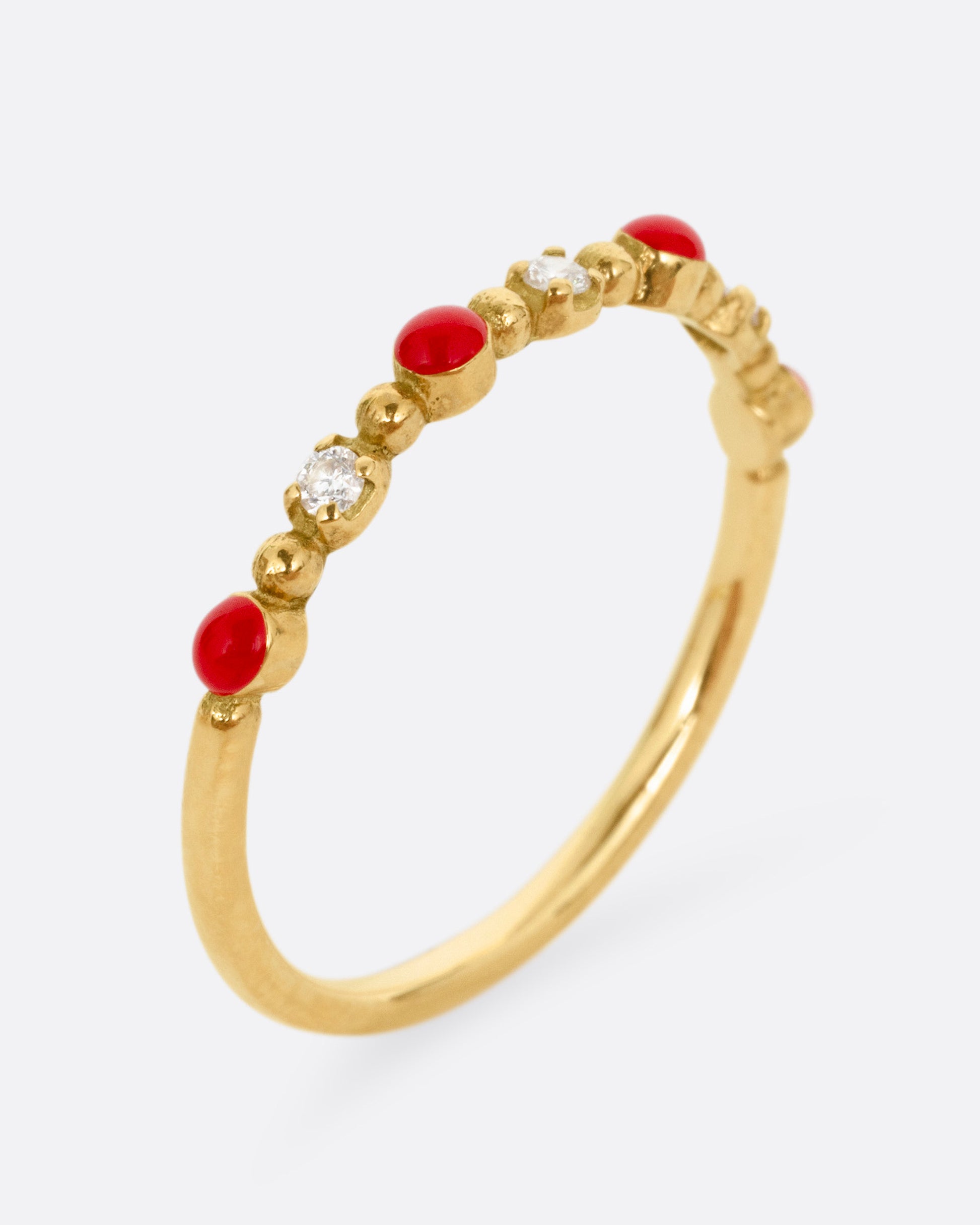 A yellow gold ring with three white diamonds and four red resin droplets, shown from the side standing up.