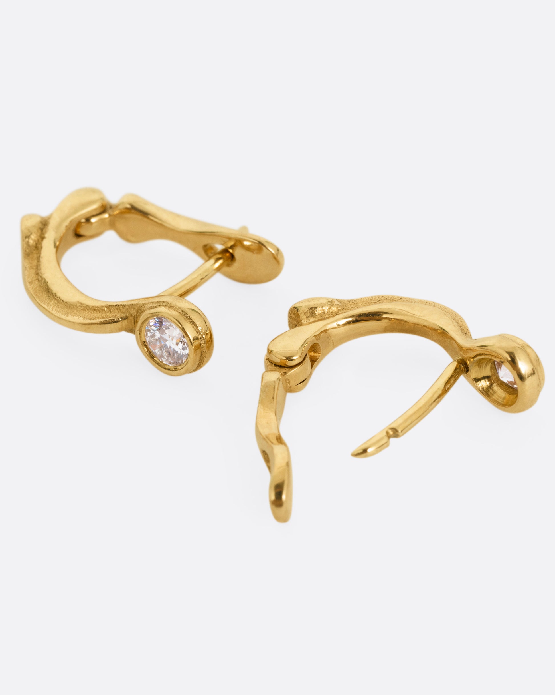 A pair of yellow gold hoop earrings with brilliant cut diamonds, shown lying on their sides with one hoop open.