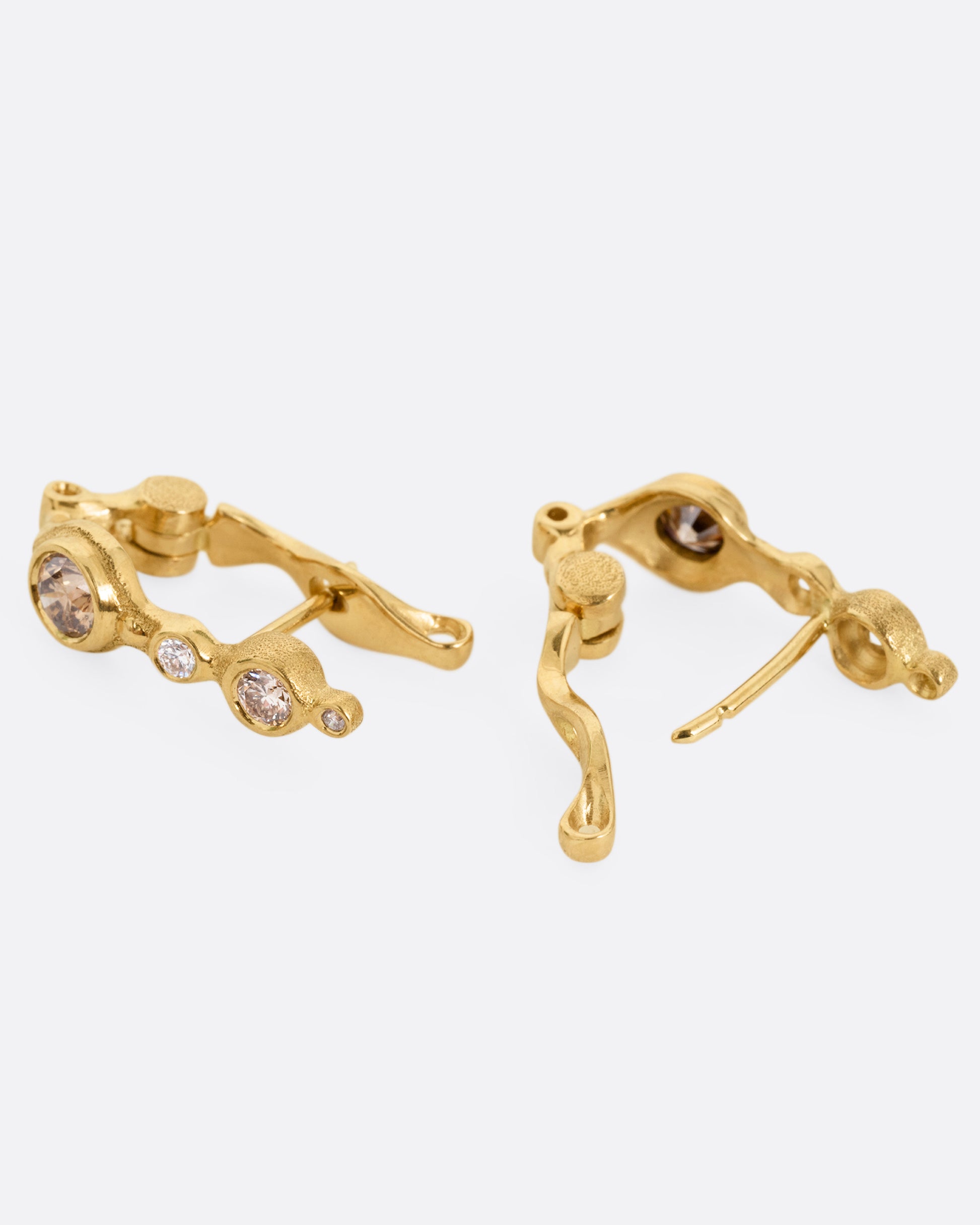 A pair of yellow gold hoop earrings with white and brown diamonds of varying shades and sizes, shown lying on their sides, with one open.