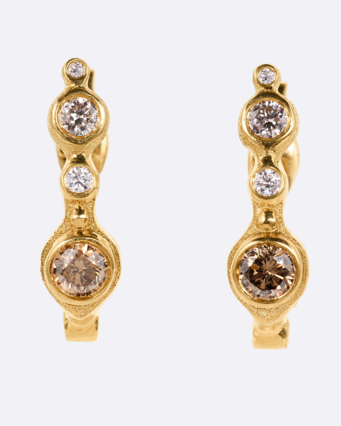 A pair of yellow gold hoop earrings with white and brown diamonds of varying shades and sizes, shown from the front.