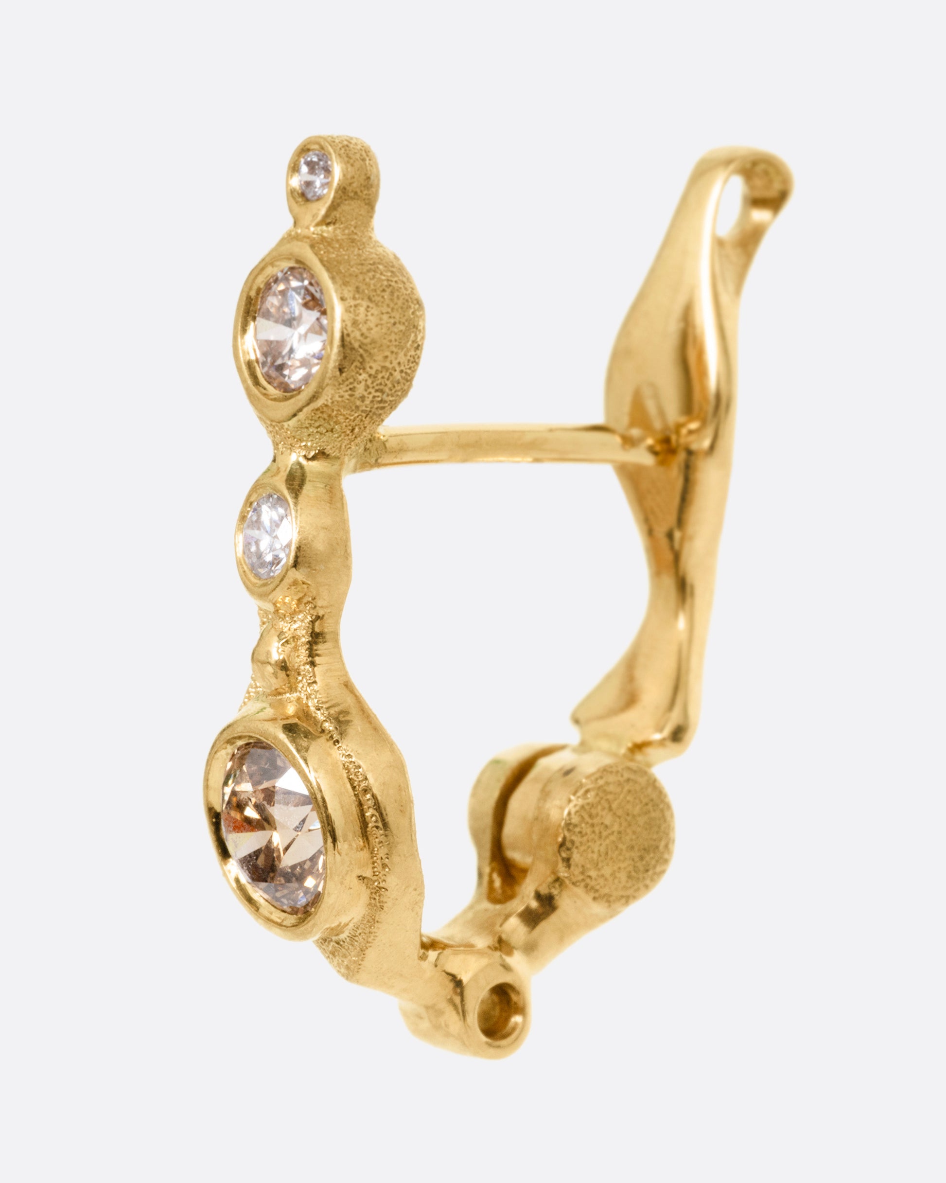 A yellow gold hoop earring with white and brown diamonds of varying shades and sizes, shown from the side.