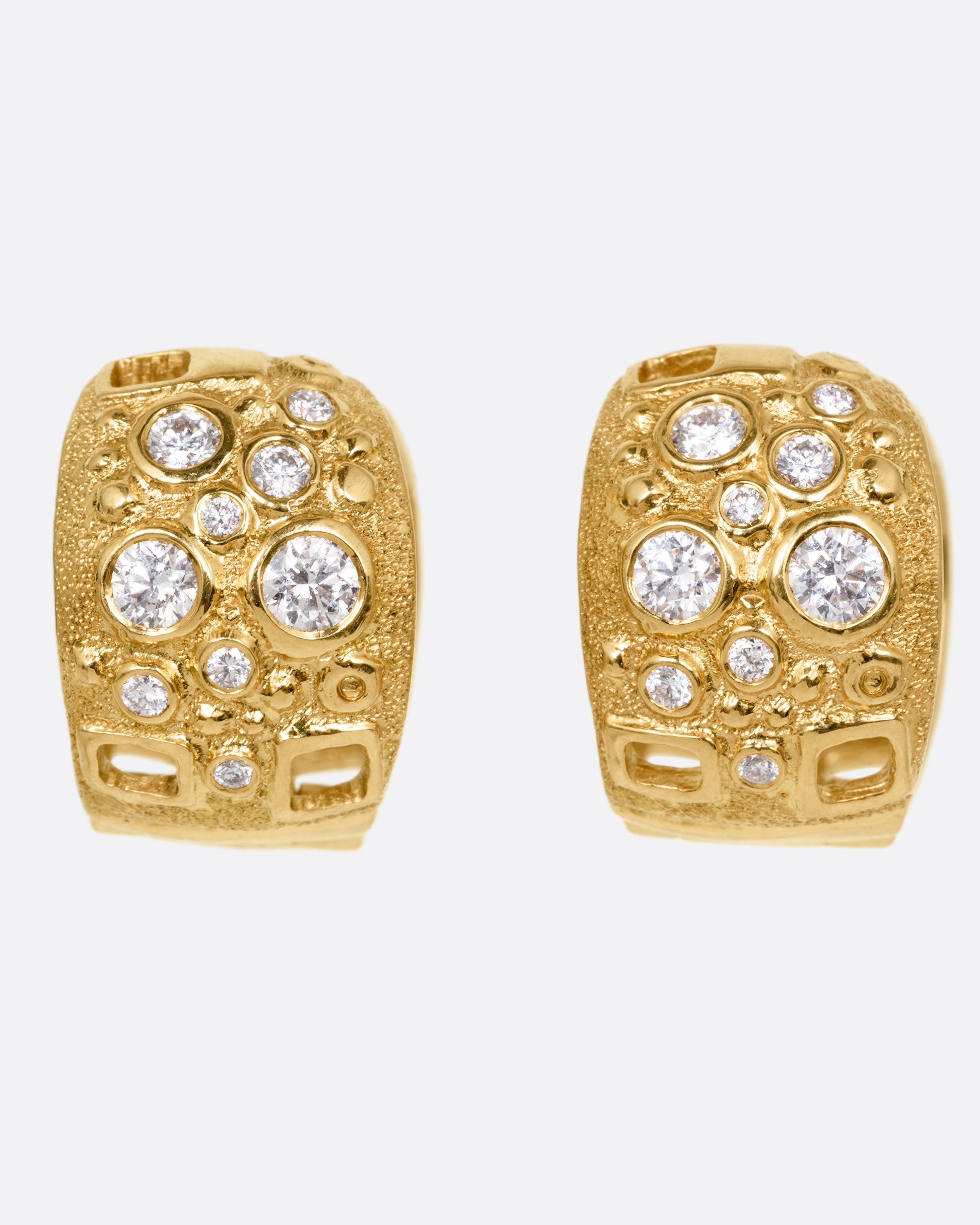 A pair of wide yellow gold huggie hoops with diamonds of varying sizes and small rectangular cutouts, shown from the front.