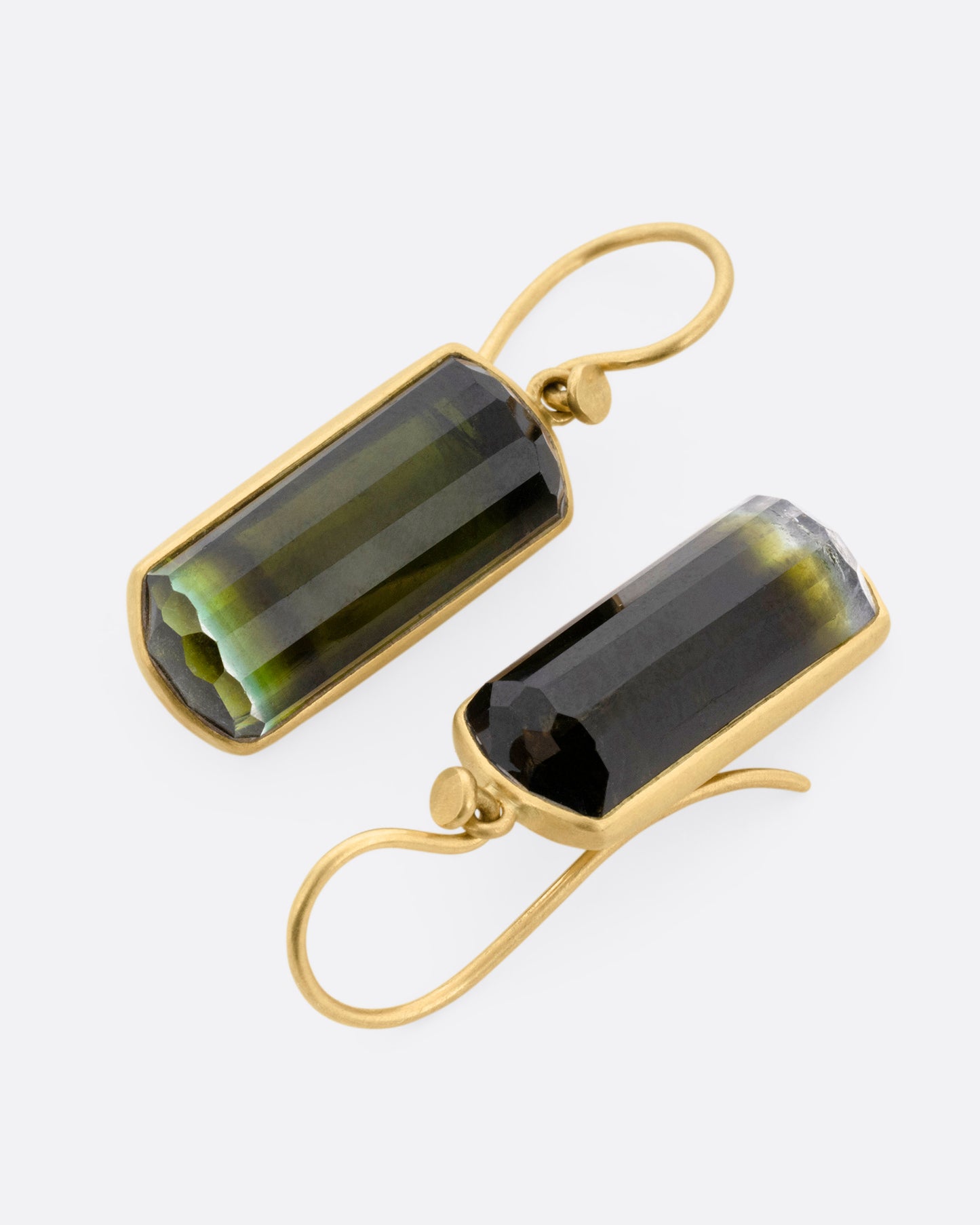 A pair of yellow gold drop earrings with bicolor barrel cut green tourmalines, shown lying flat.