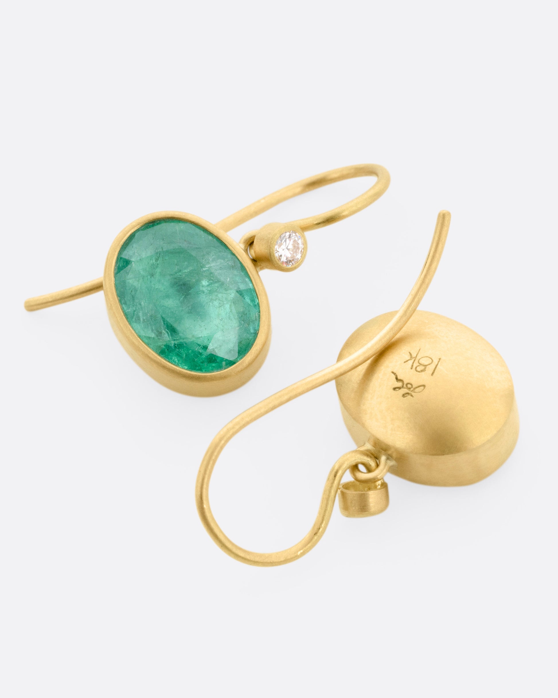 A pair of yellow gold drop earrings with Colombian emeralds and diamond accents, shown lying flat.