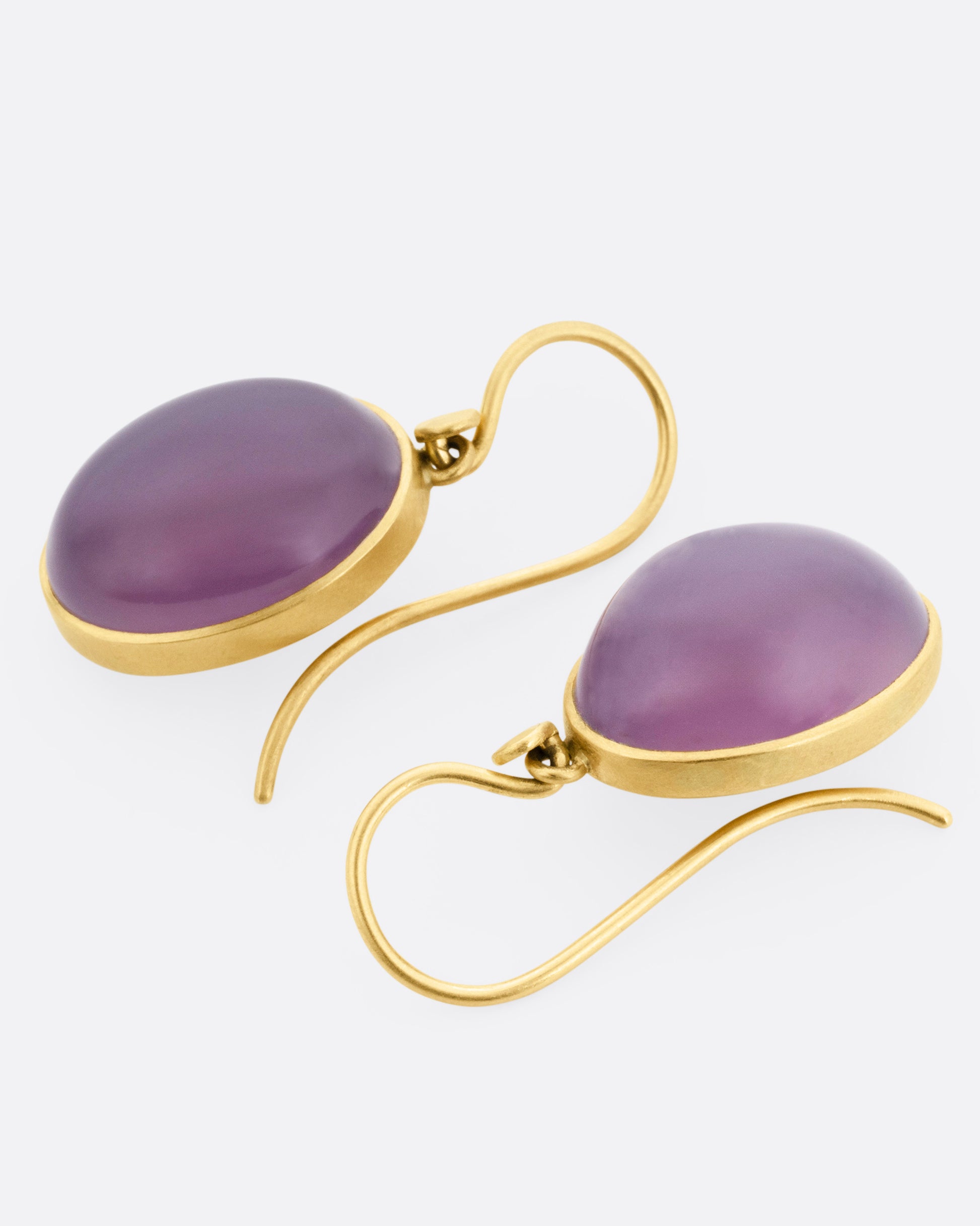 A pair of yellow gold earrings with purple chalcedony drops, shown lying flat.