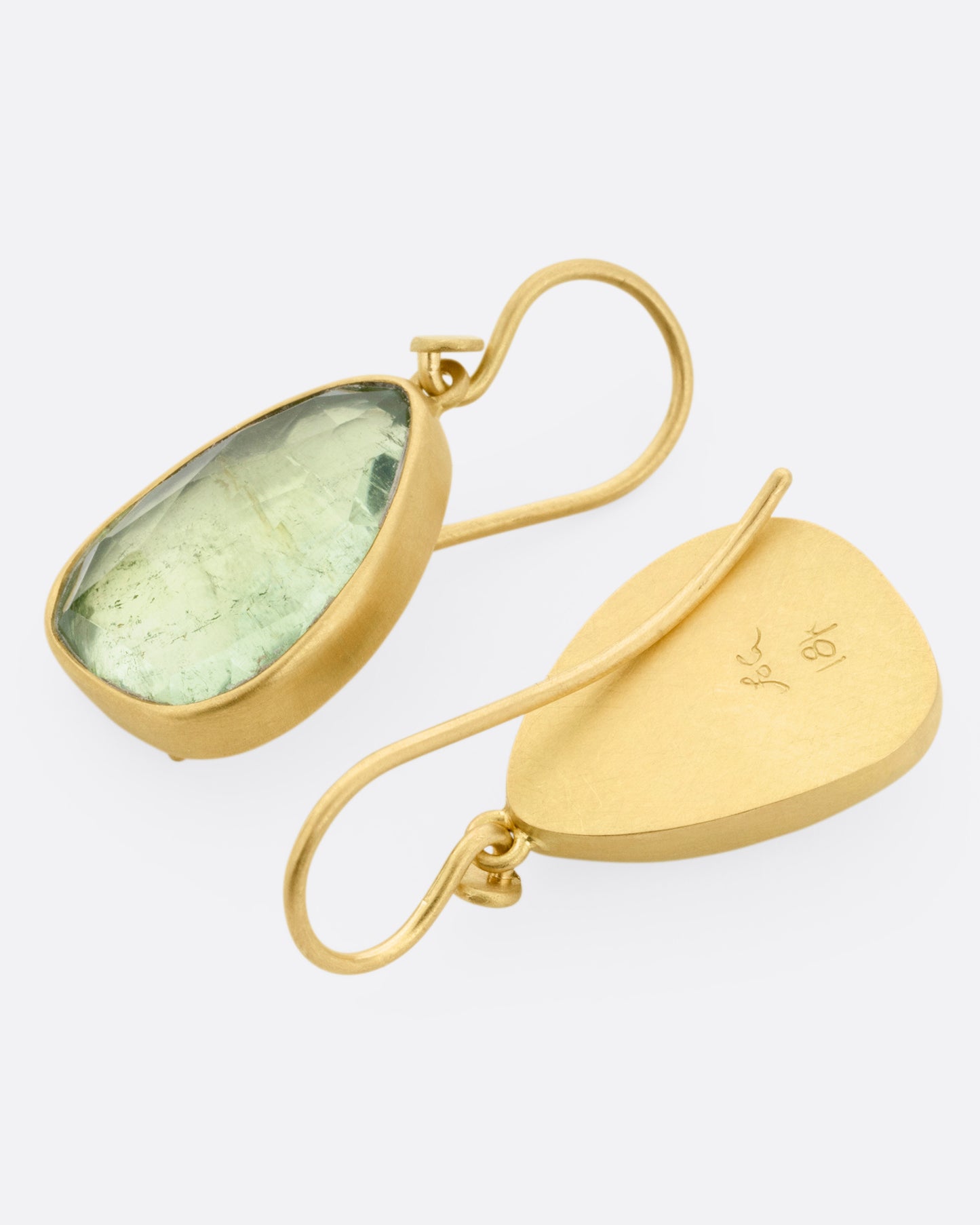A pair of yellow gold drop earrings with pale green tourmalines, shown lying flat with one earring facing back, the  other front.