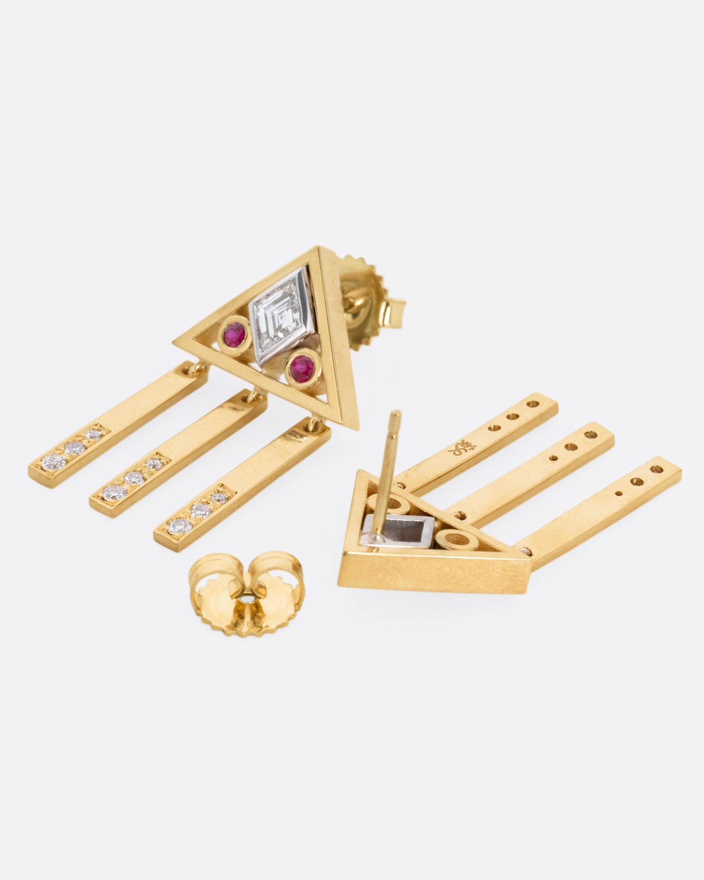 A yellow gold pair of stud back earrings with triangular tops set with lozenge cut diamonds flanked by rubies, and three free moving diamond studded bars on each base. One earring is shown from the front, the other from the back, open.