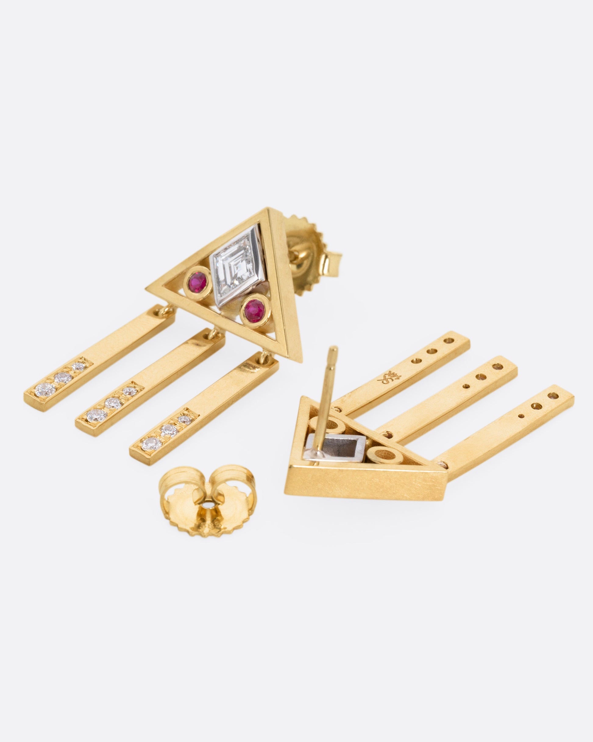 A yellow gold pair of stud back earrings with triangular tops set with lozenge cut diamonds flanked by rubies, and three free moving diamond studded bars on each base. One earring is shown from the front, the other from the back, open.