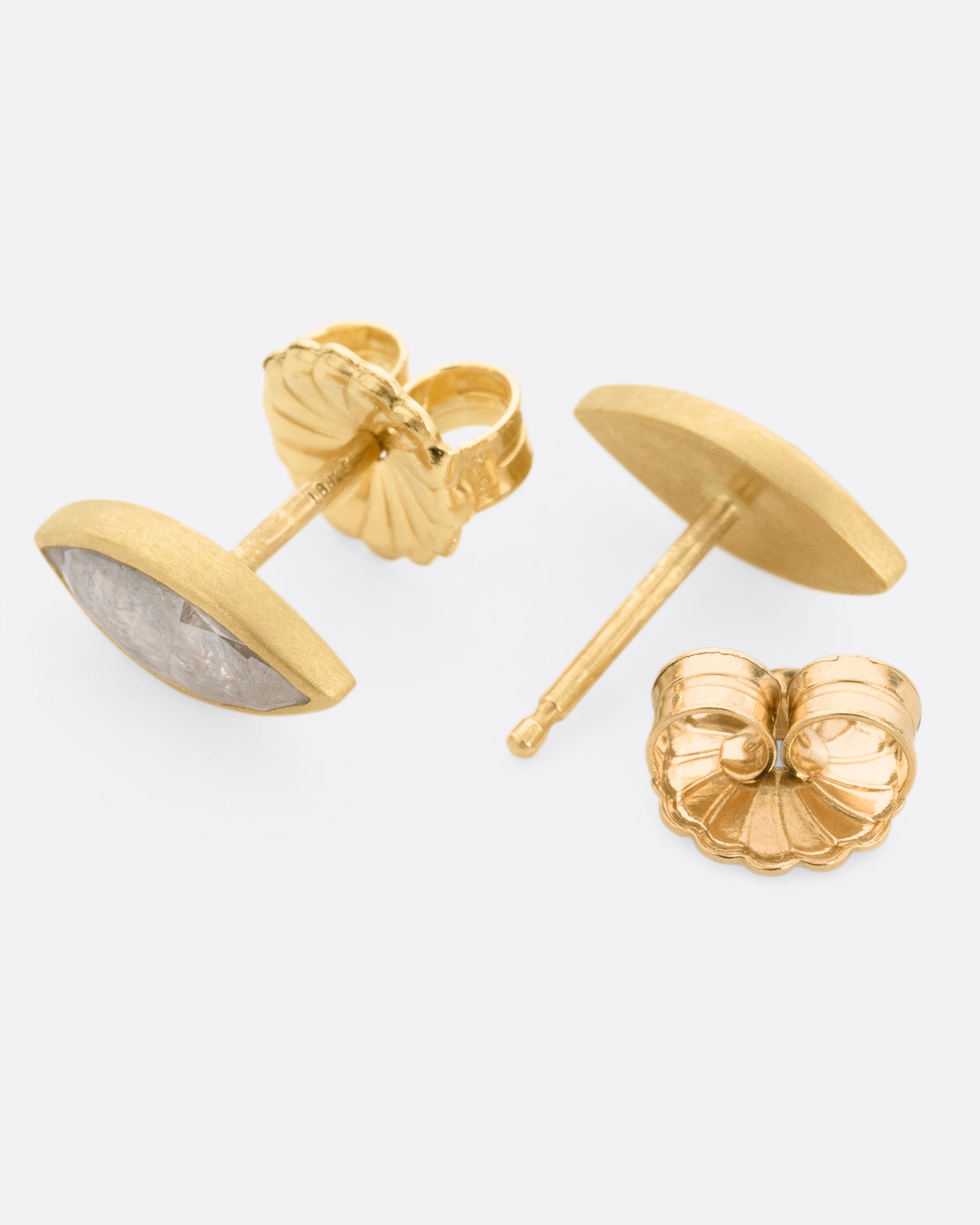 A pair of yellow gold navette diamond earrings, shown lying of their sides, with one earring open.