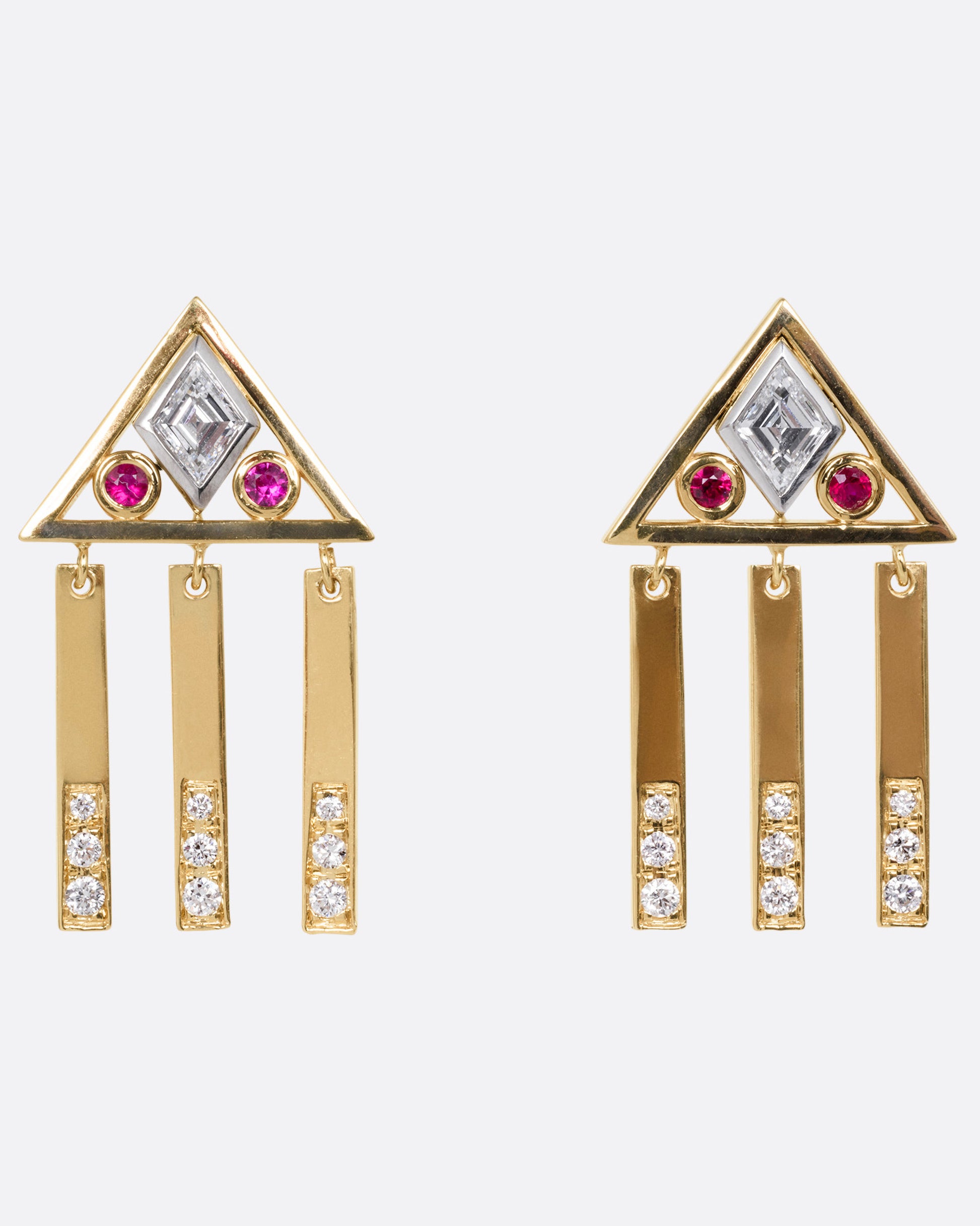 A yellow gold pair of stud back earrings with triangular tops set with lozenge cut diamonds flanked by rubies, and three free moving diamond studded bars on each base. Shown from the front.