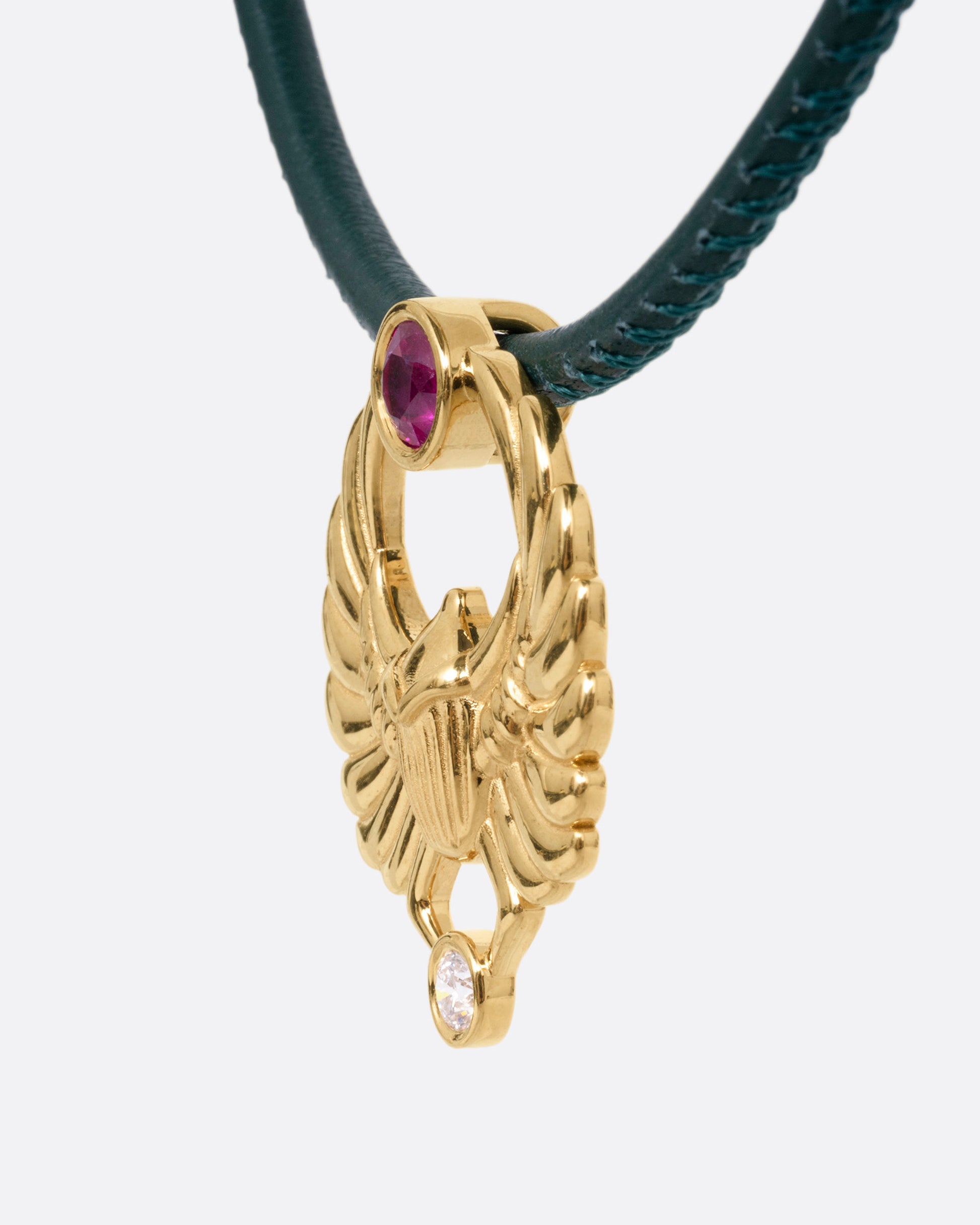 A yellow gold scarab pendant with a ruby and diamond, suspended from a green leather choker cord. Shown from the side.