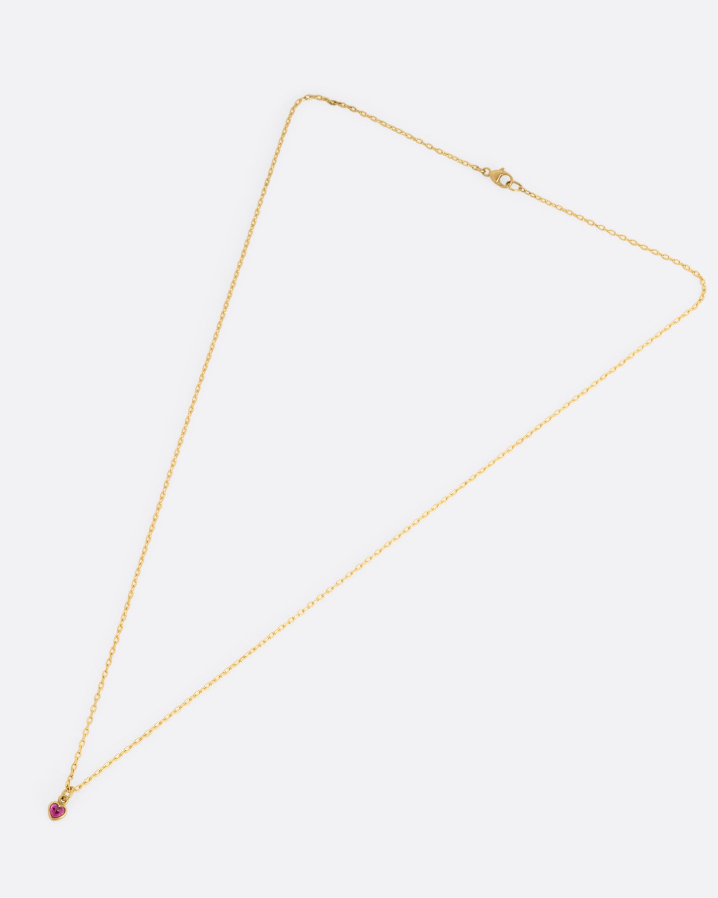 A yellow gold cable chain necklace with a tiny dimensional ruby heart, shown from the front.