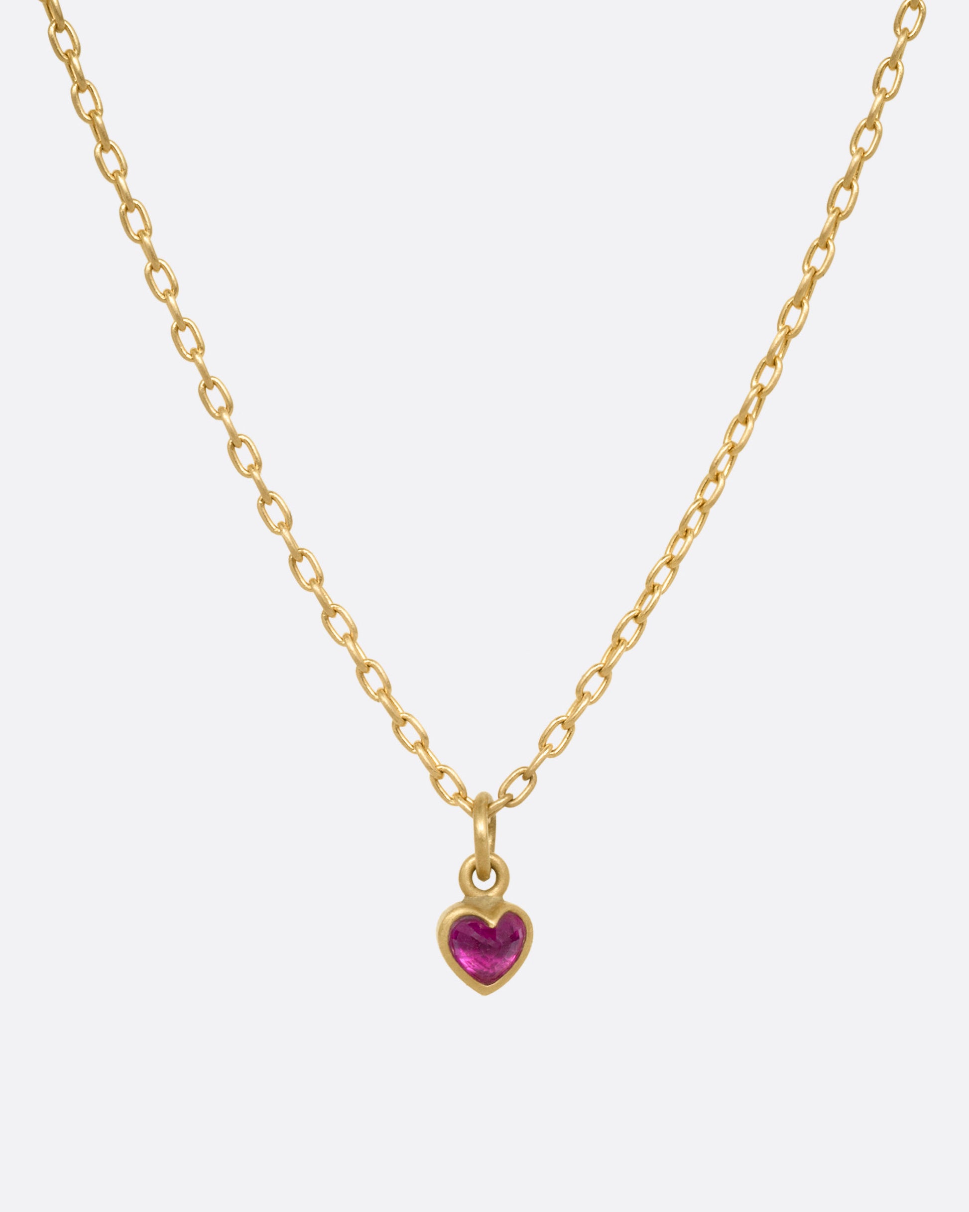 A yellow gold cable chain necklace with a tiny dimensional ruby heart, shown from the front.