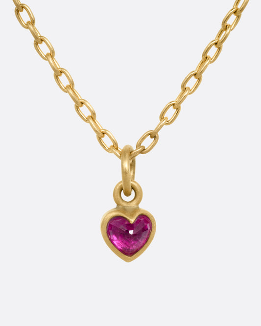 A yellow gold cable chain necklace with a tiny dimensional ruby heart, shown from the front.