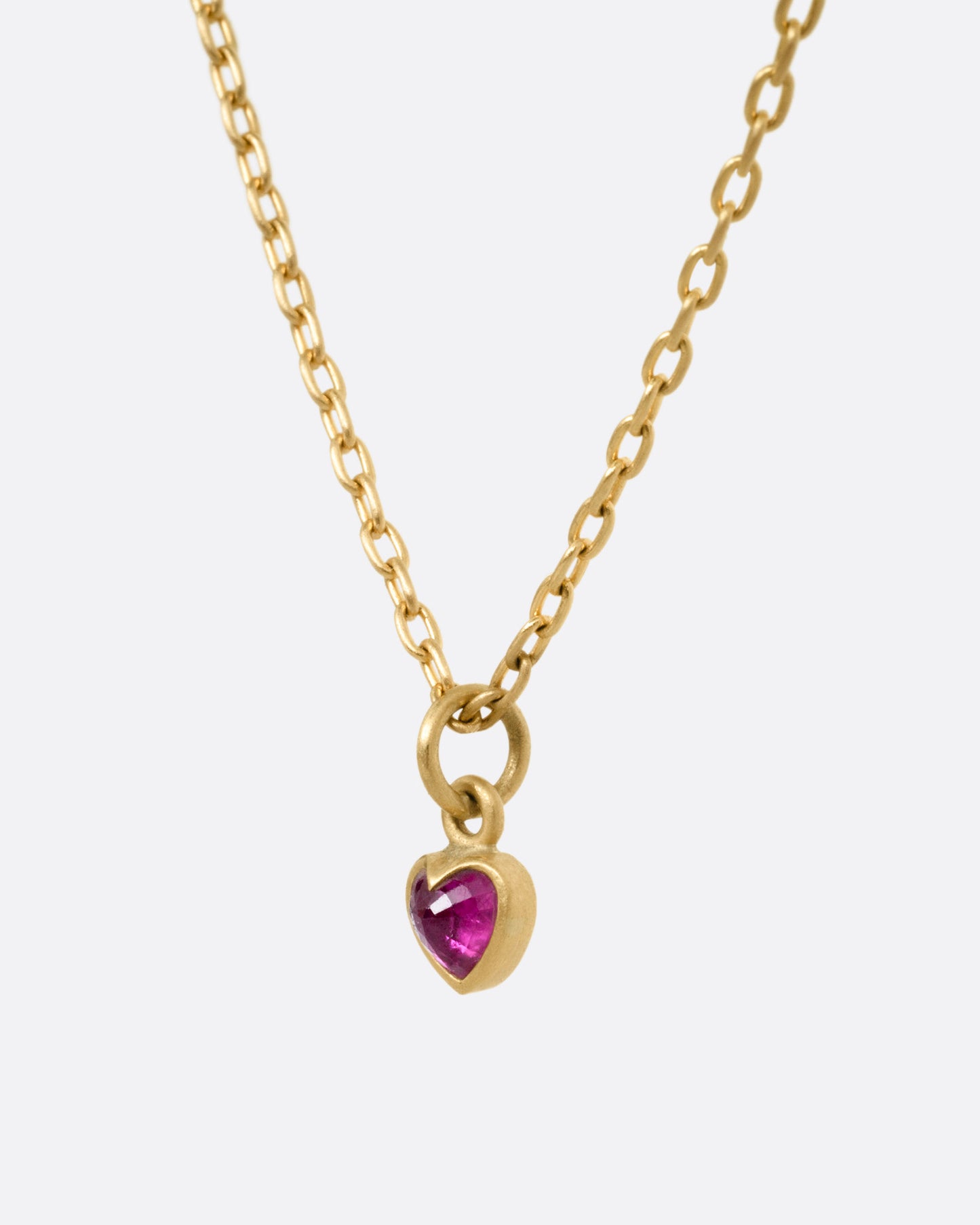 A yellow gold cable chain necklace with a tiny dimensional ruby heart, shown from the side.