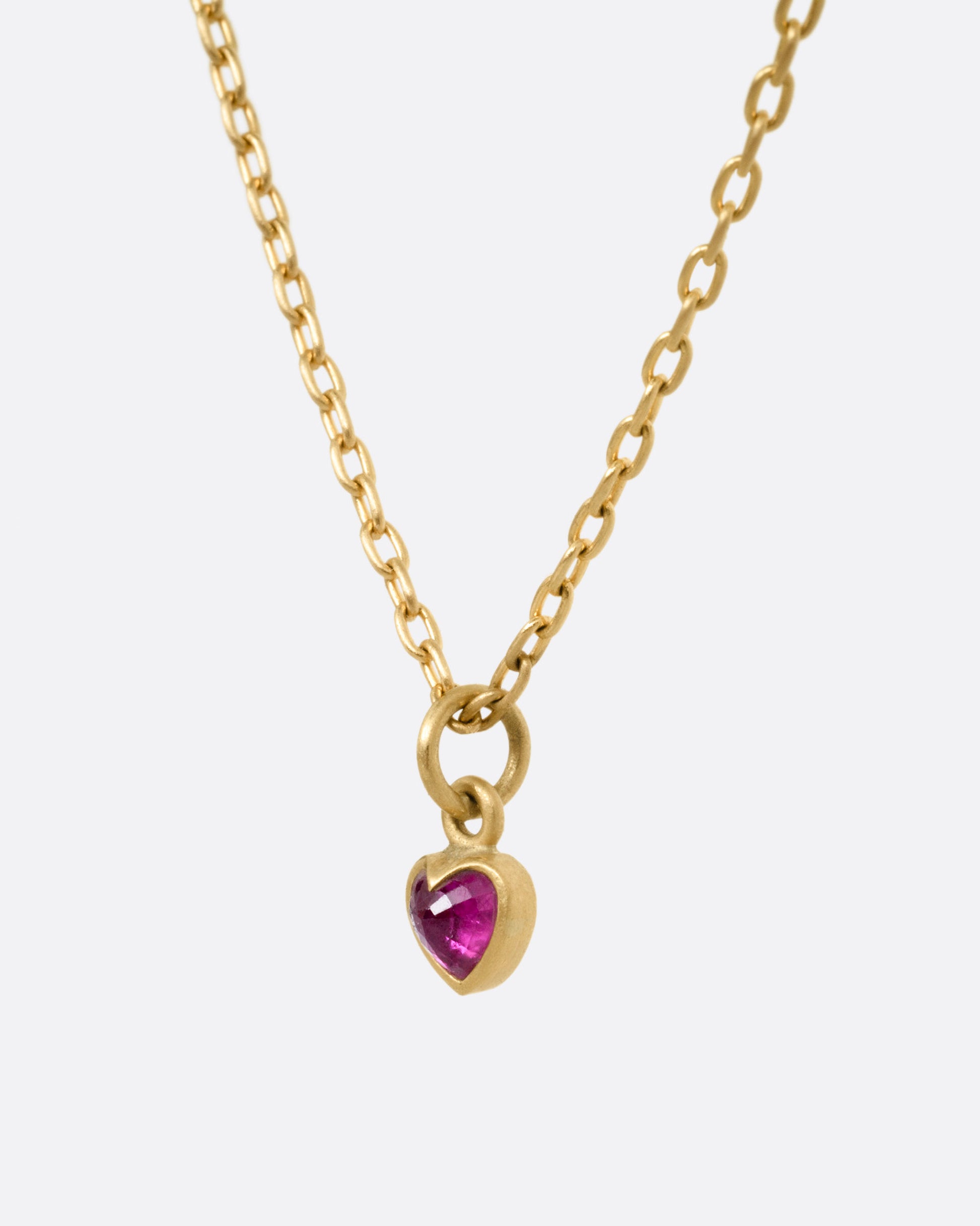 A yellow gold cable chain necklace with a tiny dimensional ruby heart, shown from the side.