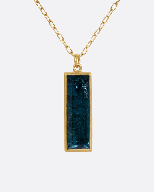 A yellow gold pendant necklace with a blue tourmaline slab, shown from the front.