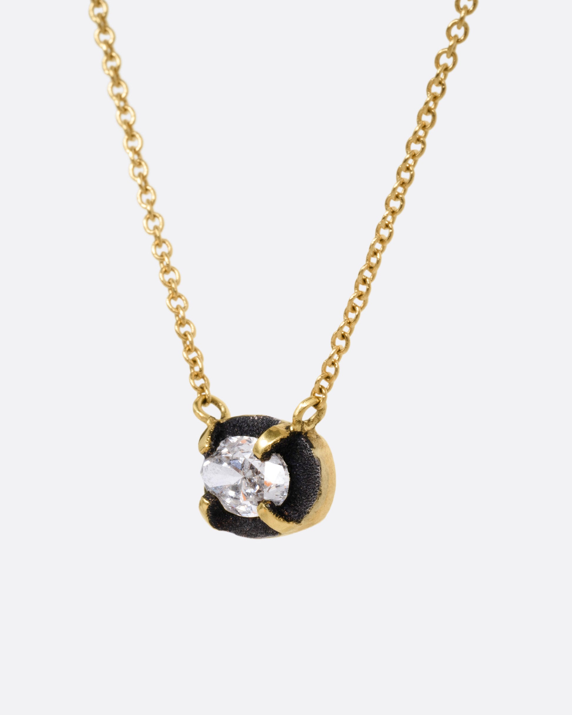 A yellow gold necklace with a pendant of darkened white gold surrounding a prong set diamond, shown from the side.