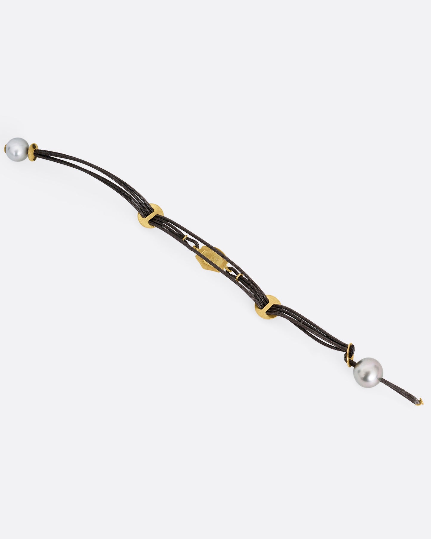 A  black cord bracelet with a diamond studded tag flanked by two gold slides and a pearl closure. Shown open from the back.