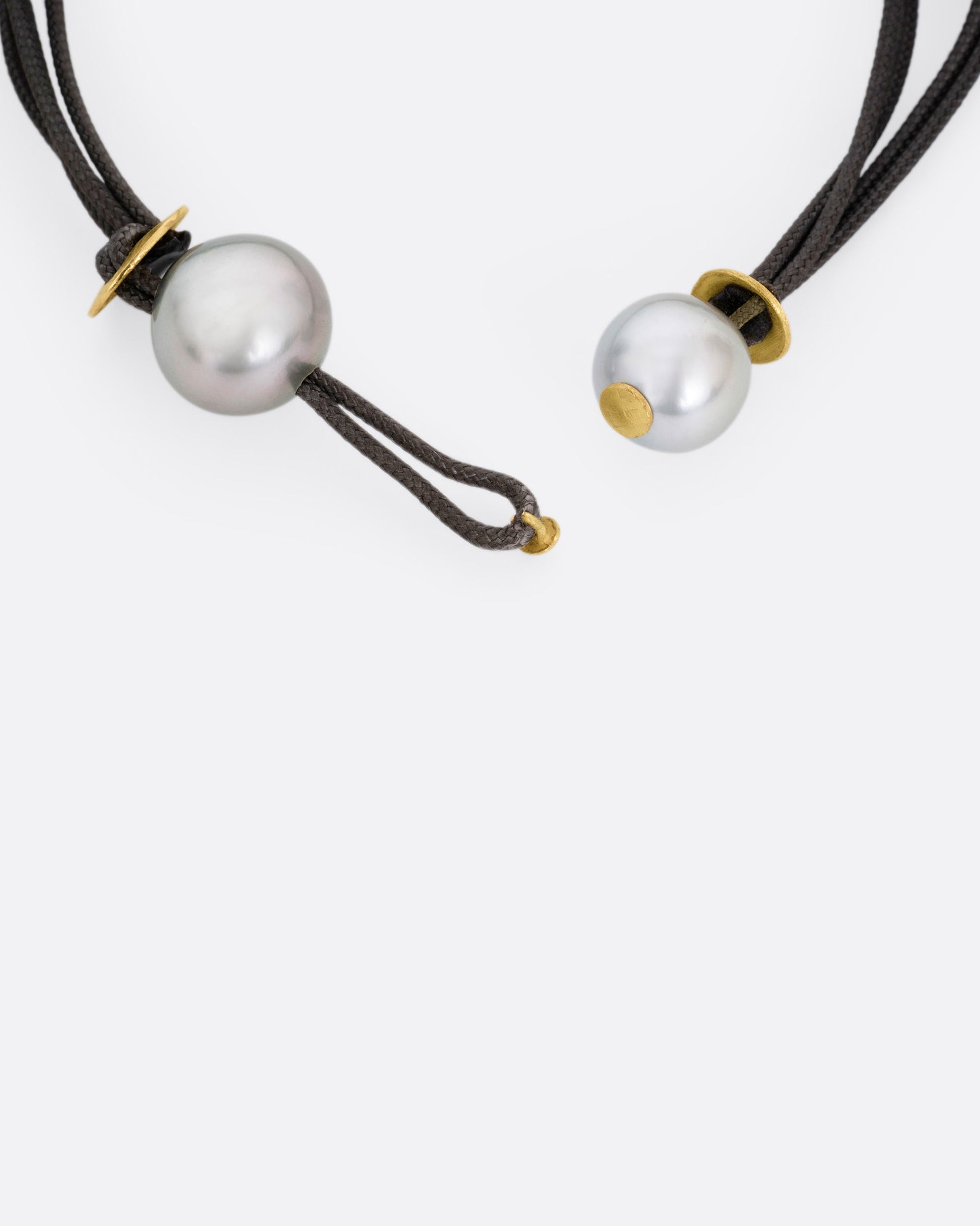 A close up of the pearl closure on a black cord bracelet. 